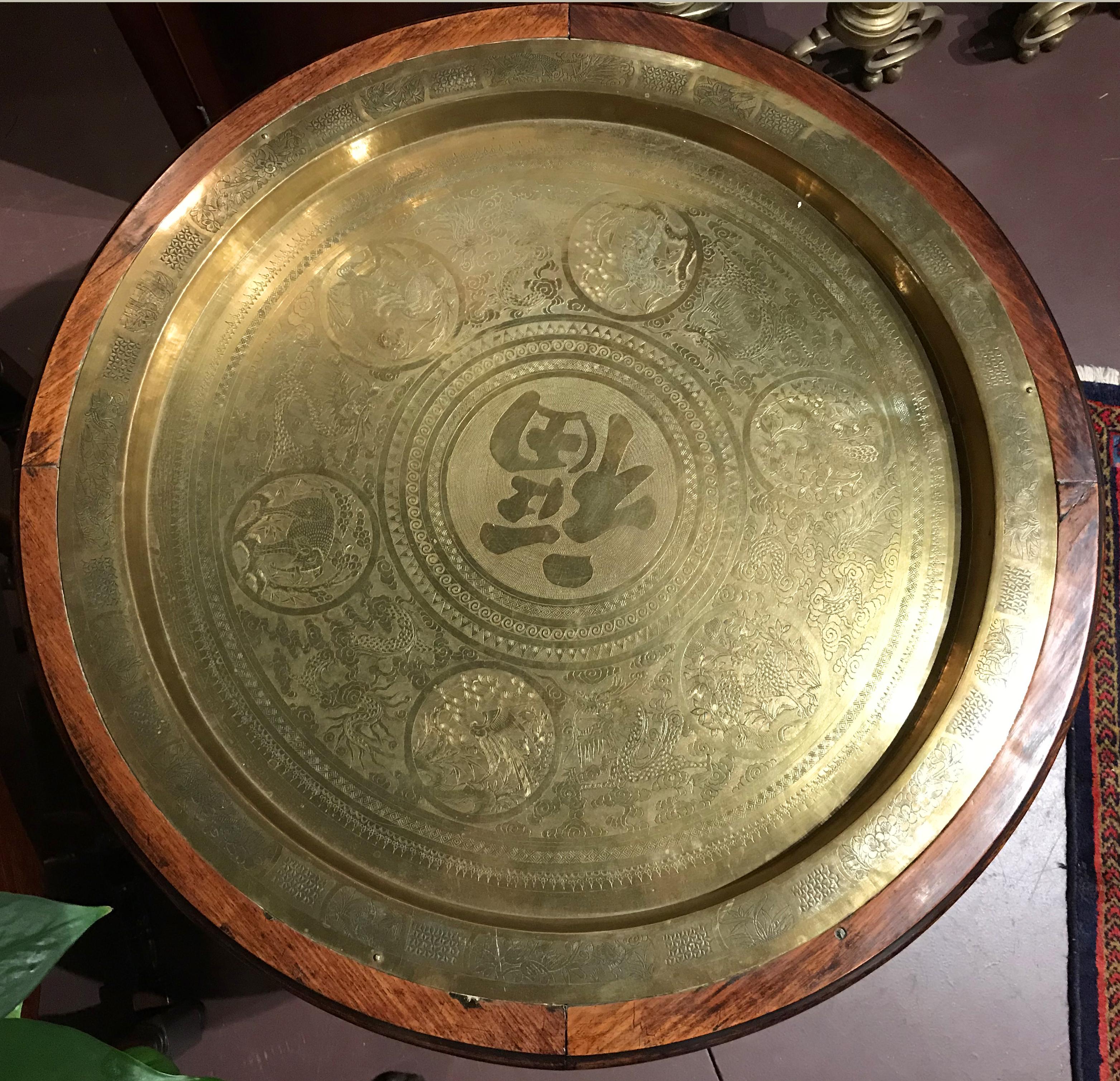 A fine reticulated foliate carved Chinese hardwood folding table with removable brass tray top encased in a wood border. The tray is decorated with a central Chinese character, surrounded by featured round animal scenes, with dragons in between each