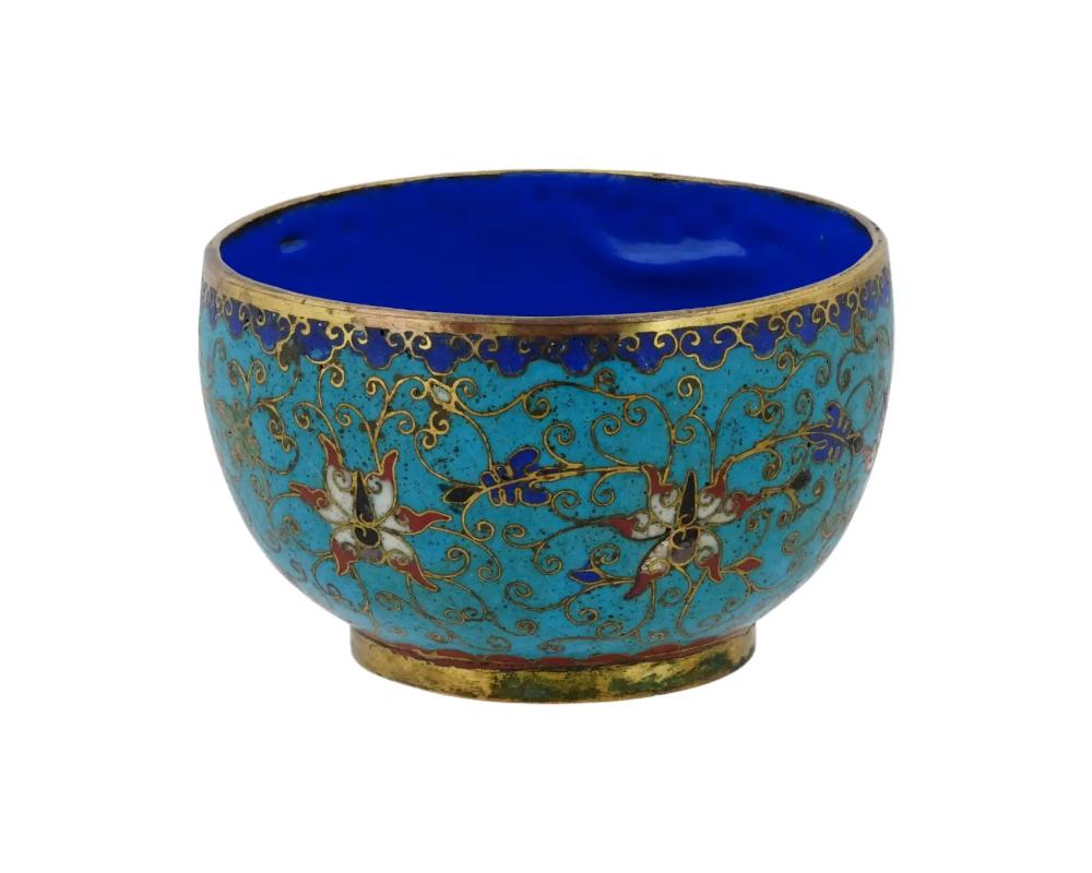 An antique footed Chinese, late Qing dynasty, enamel over copper bowl. The exterior of the bowl is adorned with floral, foliage and scrollwork motifs made in the Cloisonne technique. The border features a cloud ornament made in the same technique.