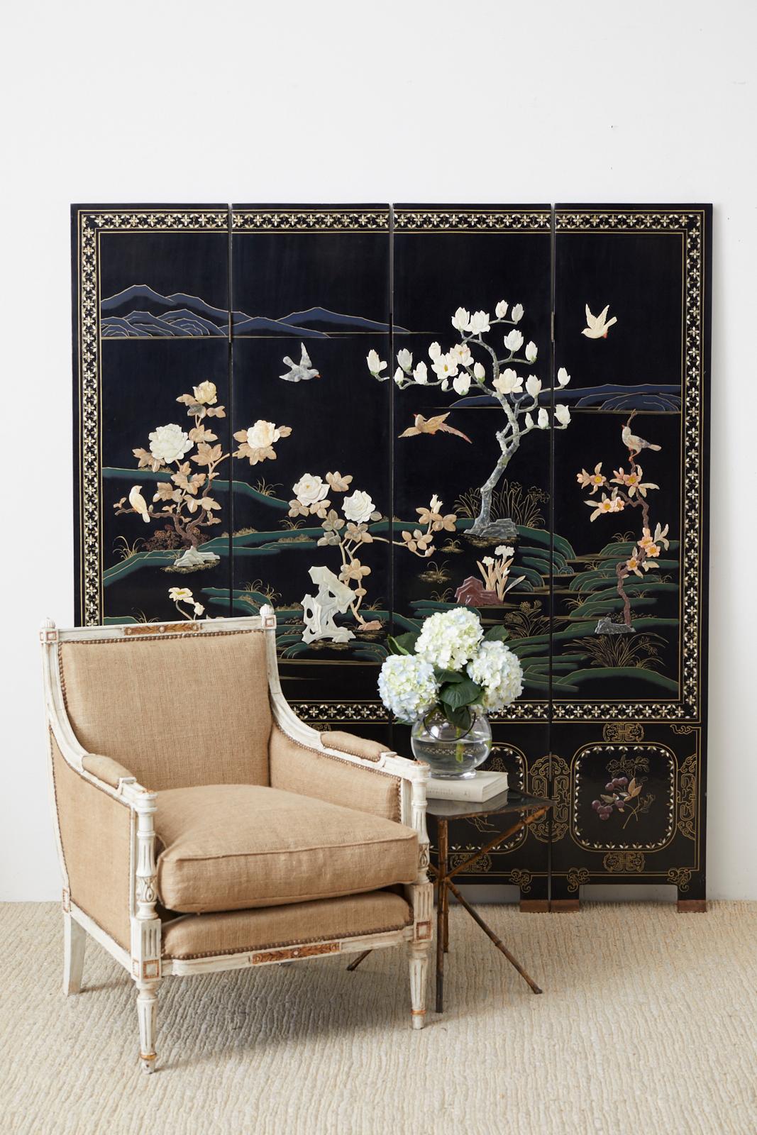 Stunning Chinese export four-panel screen depicting a colorful landscape embellished with hand carved flora and fauna in soapstone. The screen has vibrant green and blue color pigments over a black lacquer background. The border of the screen panels