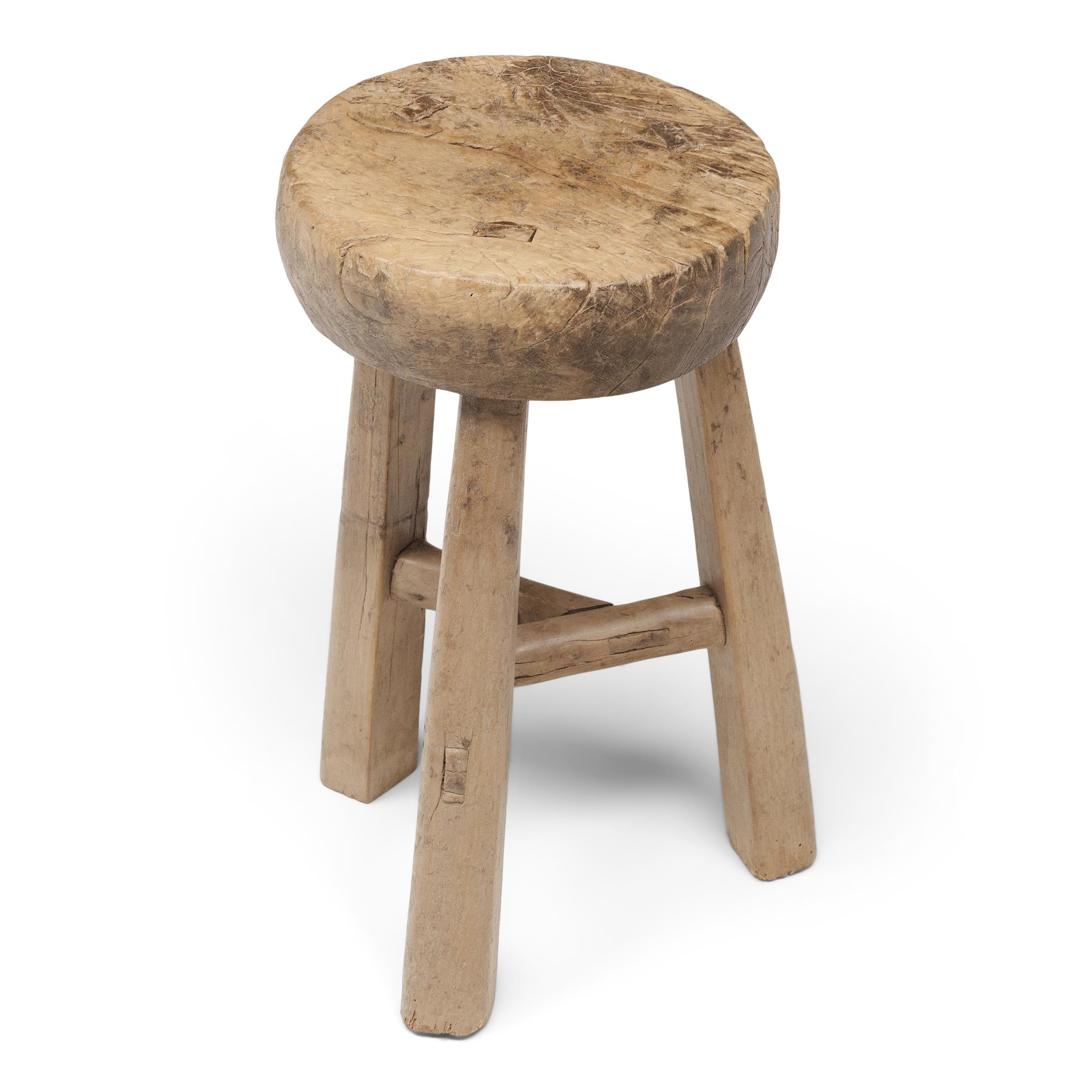 This 19th-century tri-leg stool from China's Shanxi province charms with its top-heavy form and timeworn texture. Crafted of elm with mortise-and-tenon joinery, the robust stool stands on three tapered legs linked with interlocking stretchers and