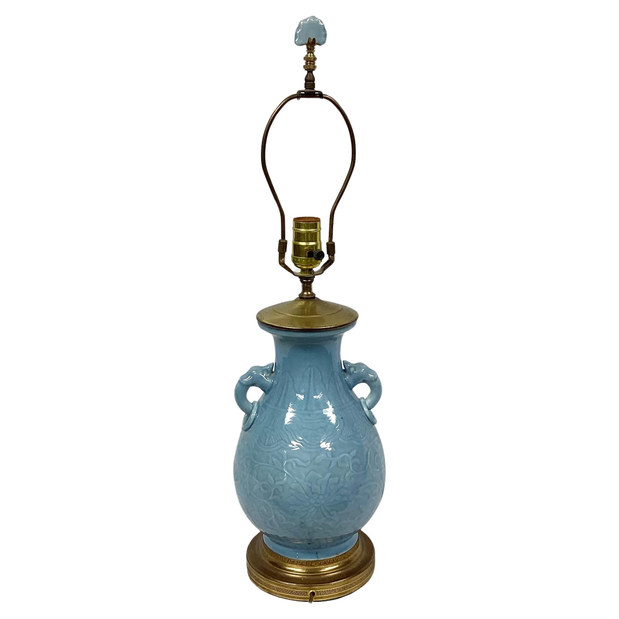 Mid 20th Century Chinese Gilt Brass Mounted Celadon porcelain lamp with molded elephant ring handles and matching finial. Harp and finial included. Molded blue floral motif throughout lamp. Mounted on gilt brass base. Measures 25.5 inches from base