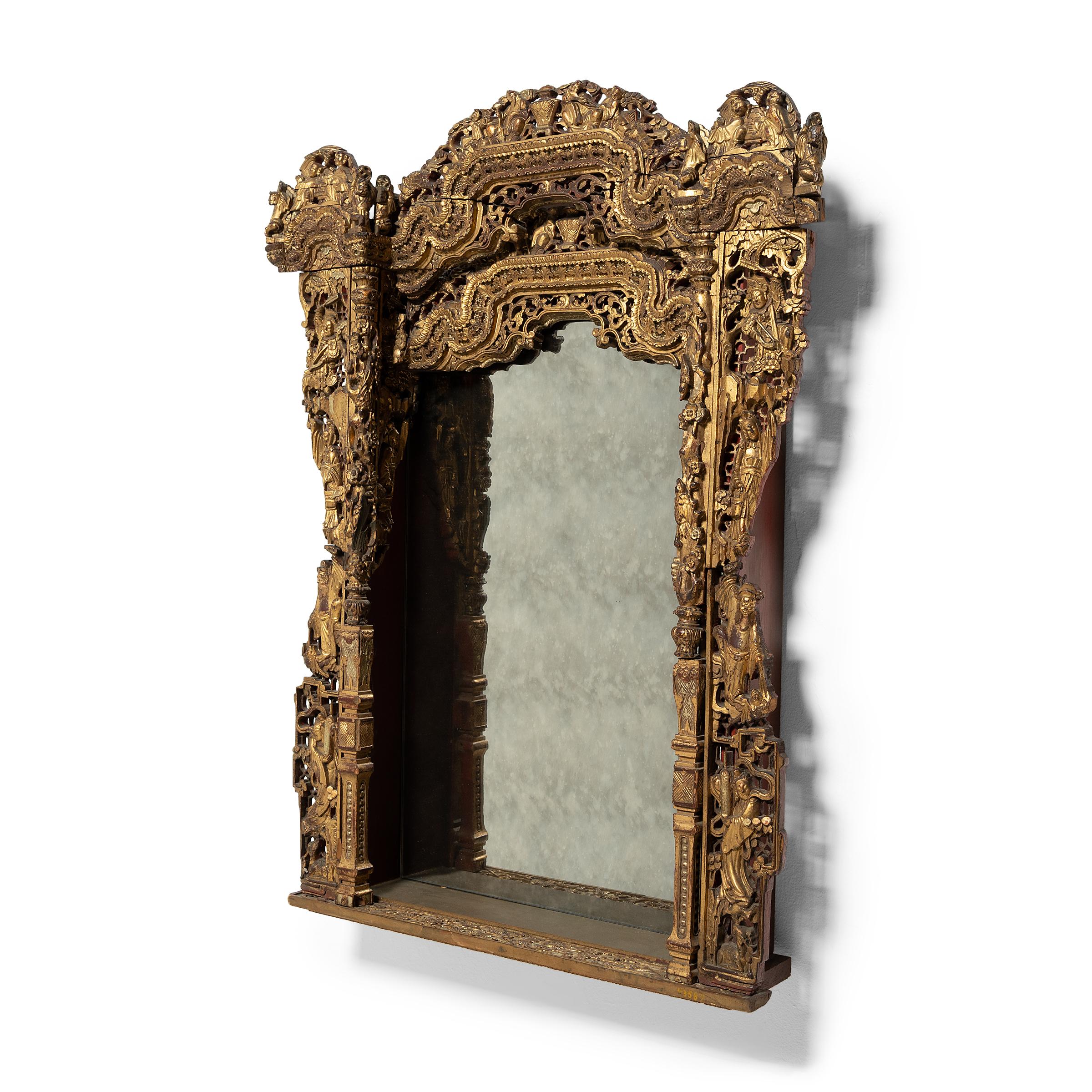 A dazzling display of intricate carvings and gilt lacquer, this fabulous wall mirror was originally an ornate shrine surround used to enclose a religious figure or shrine display. The elaborate frame is comprised of highly decorated wood panels,