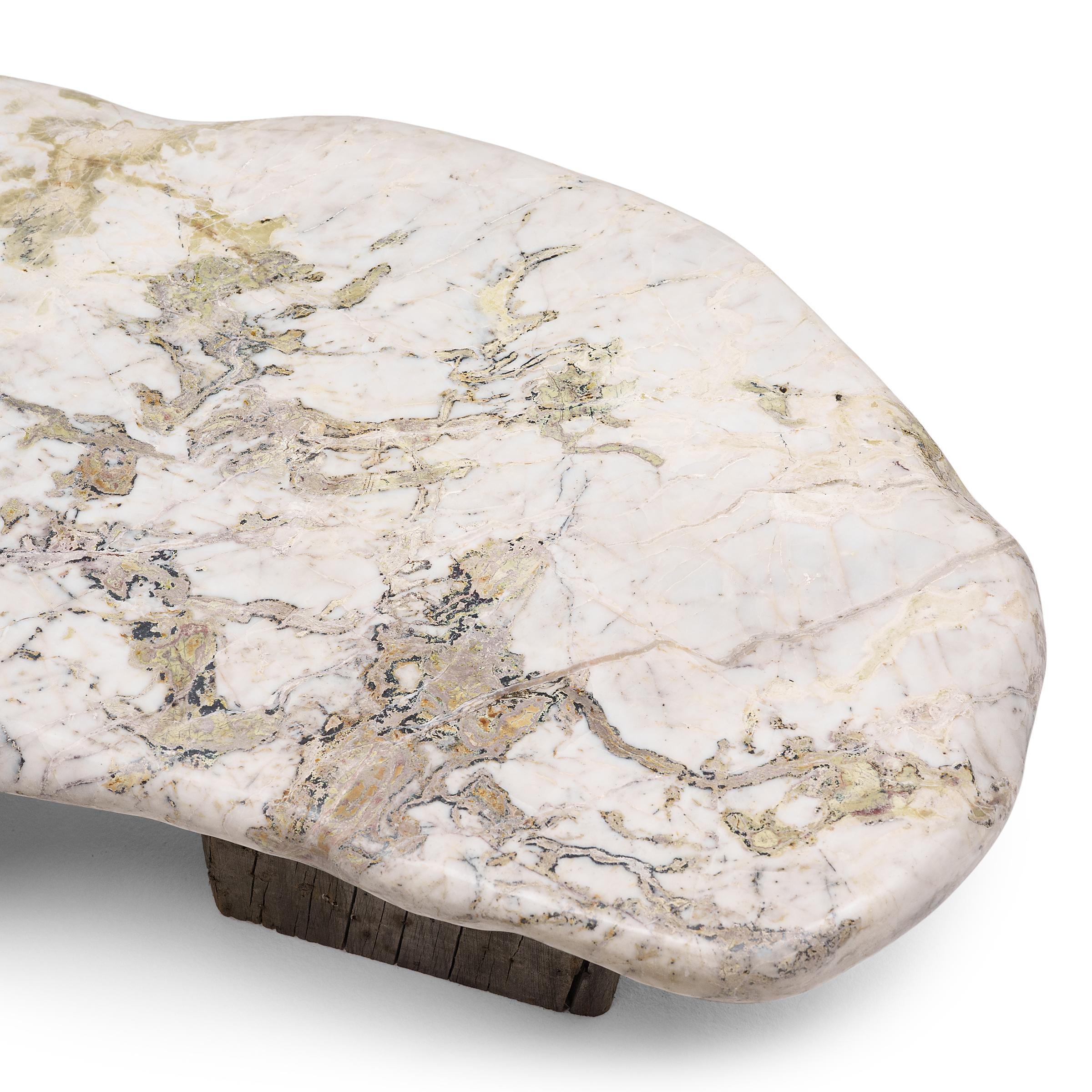 This low, stone top table exemplifies Organic Modern style with an emphasis on natural materials. The organic shape and irregular patterning of the stone slab top evokes the complexities of nature, reminiscent of a snow-covered glacier or a