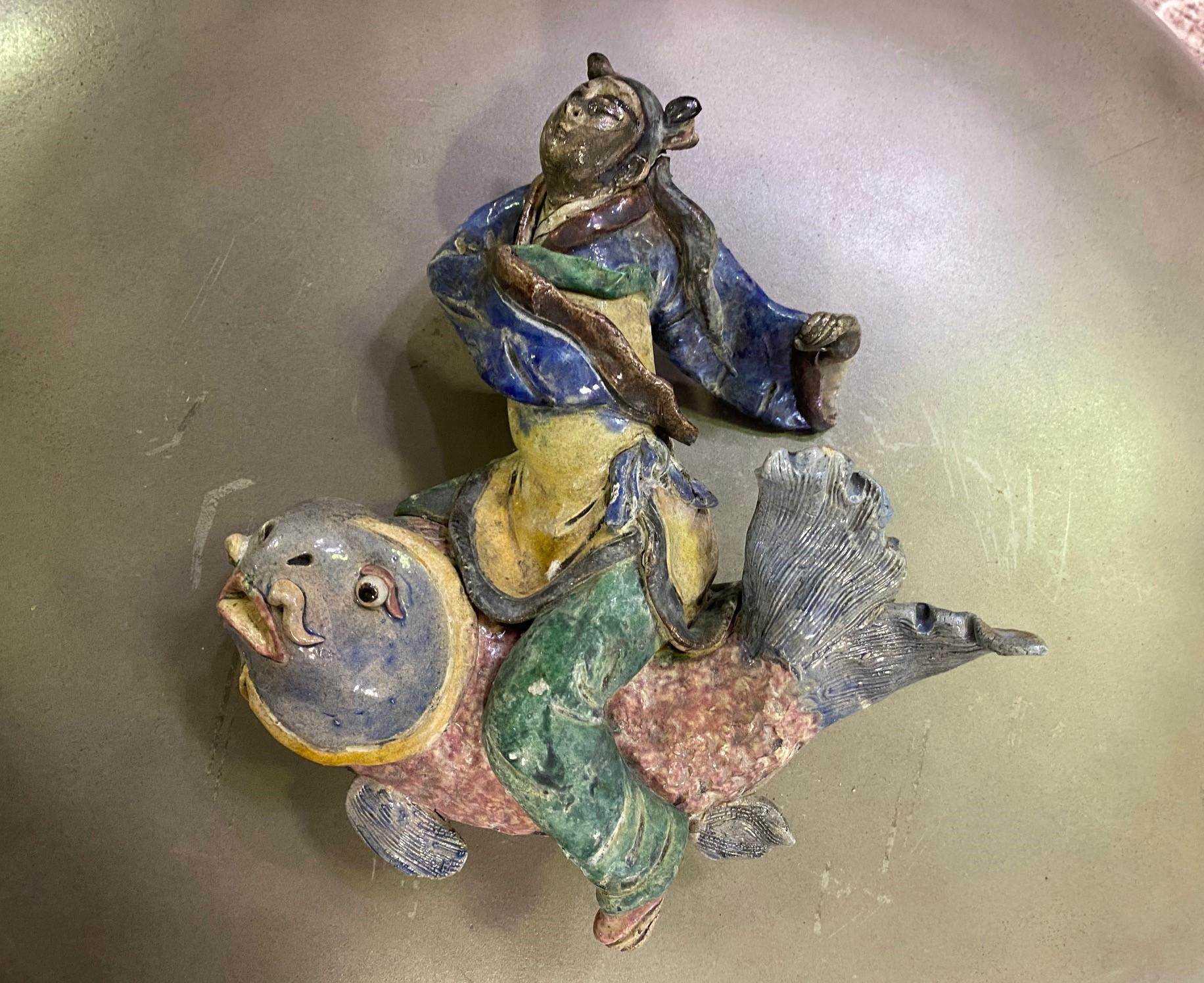 A fantastic piece. Wonderfully glazed and colored work of a seated woman with flowing robes riding a mythical fish. 

We believe this is Qing dynasty (1644-1912) but this is not our area of expertise so are listing it simply as the early 20th