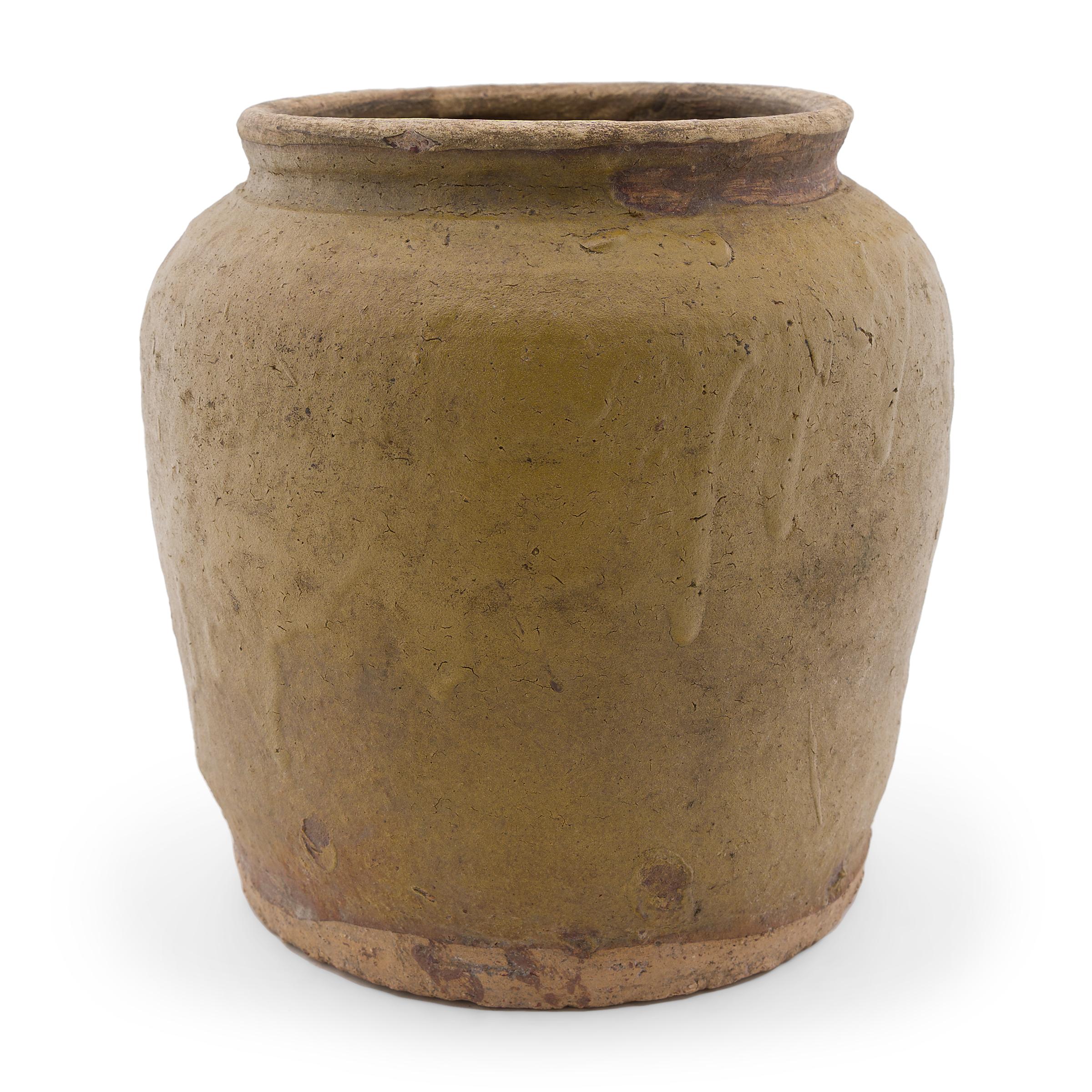 Originally used for fermenting foods and condiments in a provincial Chinese kitchen, this early 20th century terracotta jar is cloaked in a thick mustard yellow glaze. The jar has a slightly tapered form with a wide base, high shoulders, and a