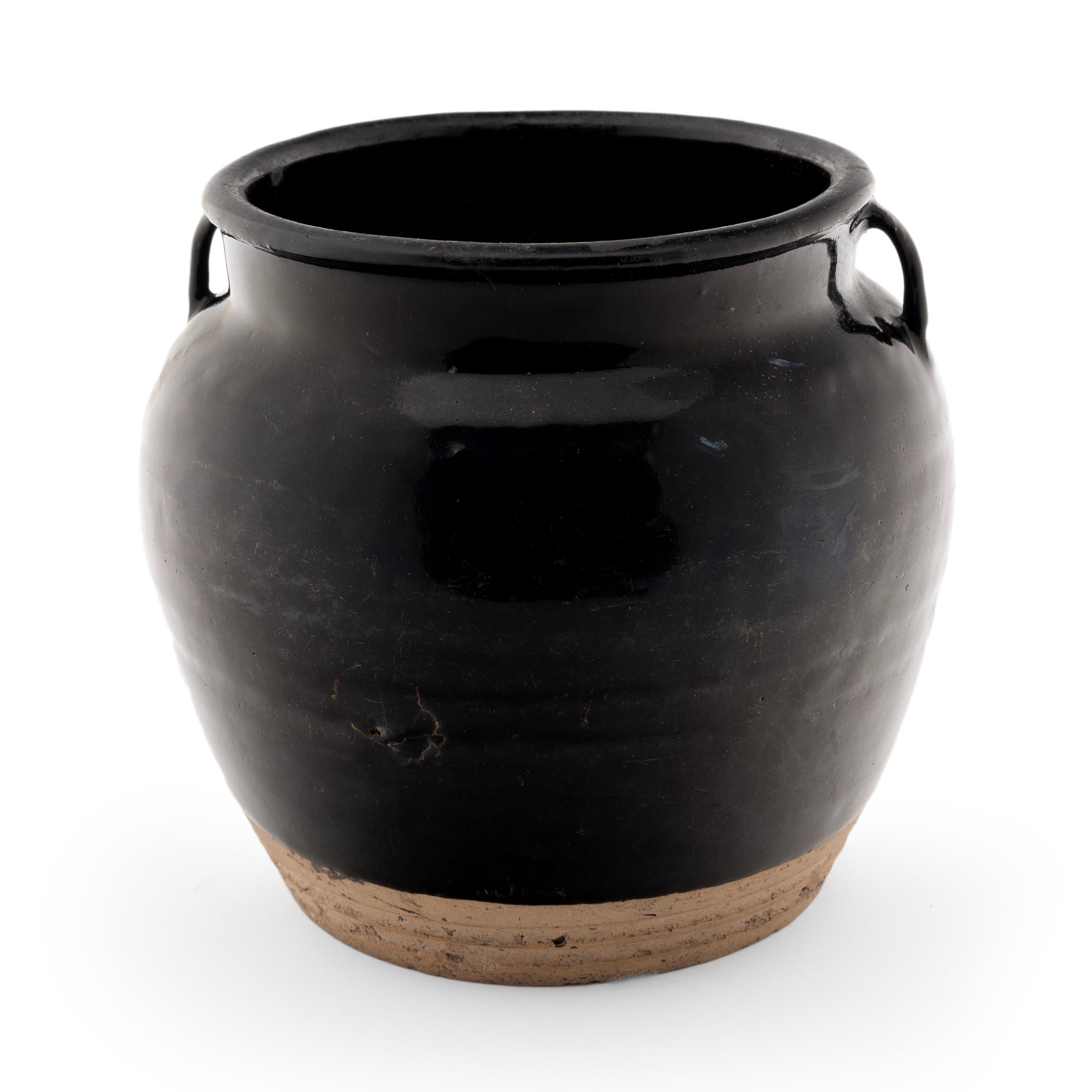 A lustrous, dark glaze clings to the squat form of this petite kitchen jar. The glazed vessel dates to the early 20th Century and was used for storing food and condiments in a Provincial Qing-dynasty kitchen, as evidenced by its interior glaze. The