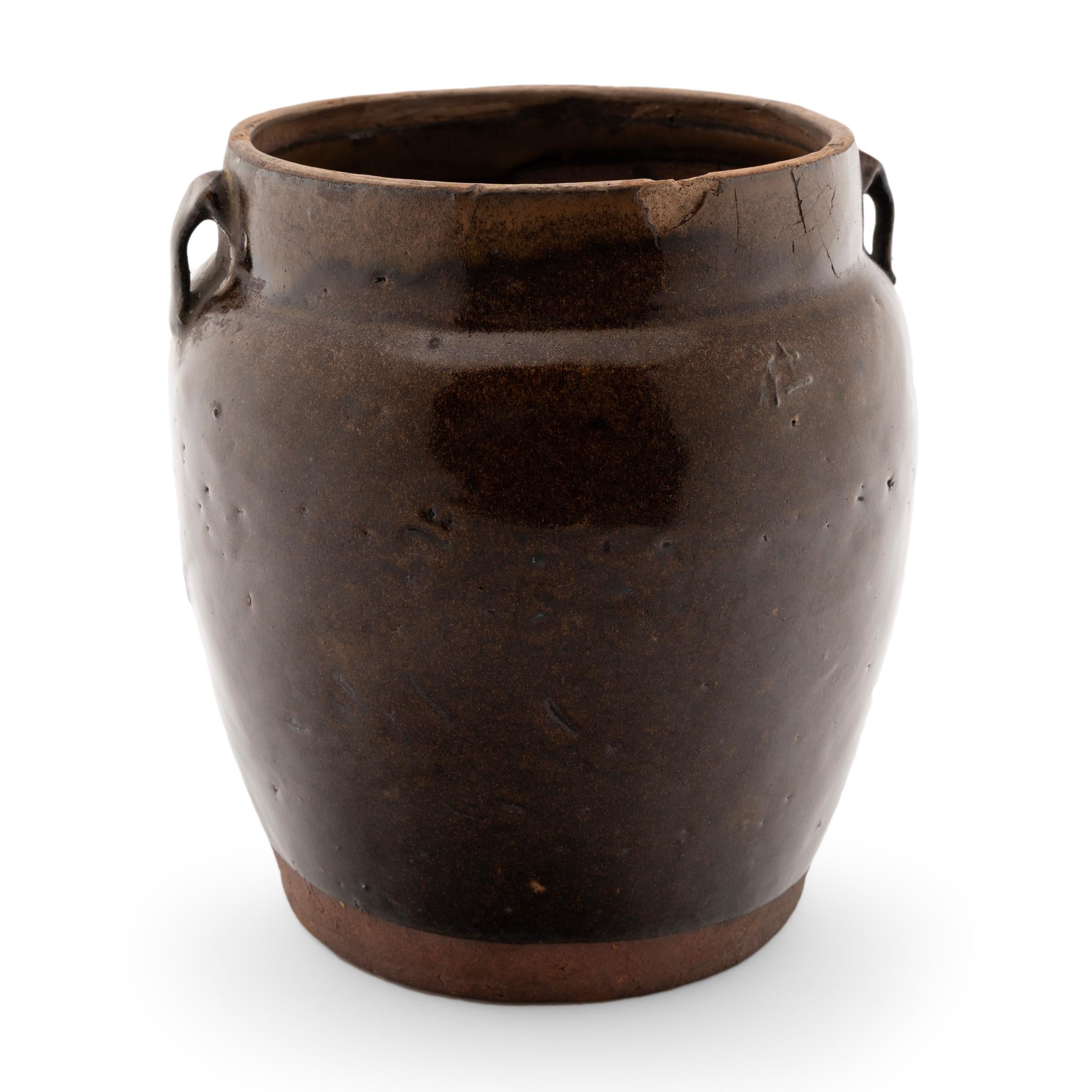 As evidenced by the interior glaze, this wide-mouth jar was once used in a Provincial Qing-dynasty kitchen for storing food and condiments. The vessel has a gently tapered form, with sloped shoulders, small strap handles and a defined, straight