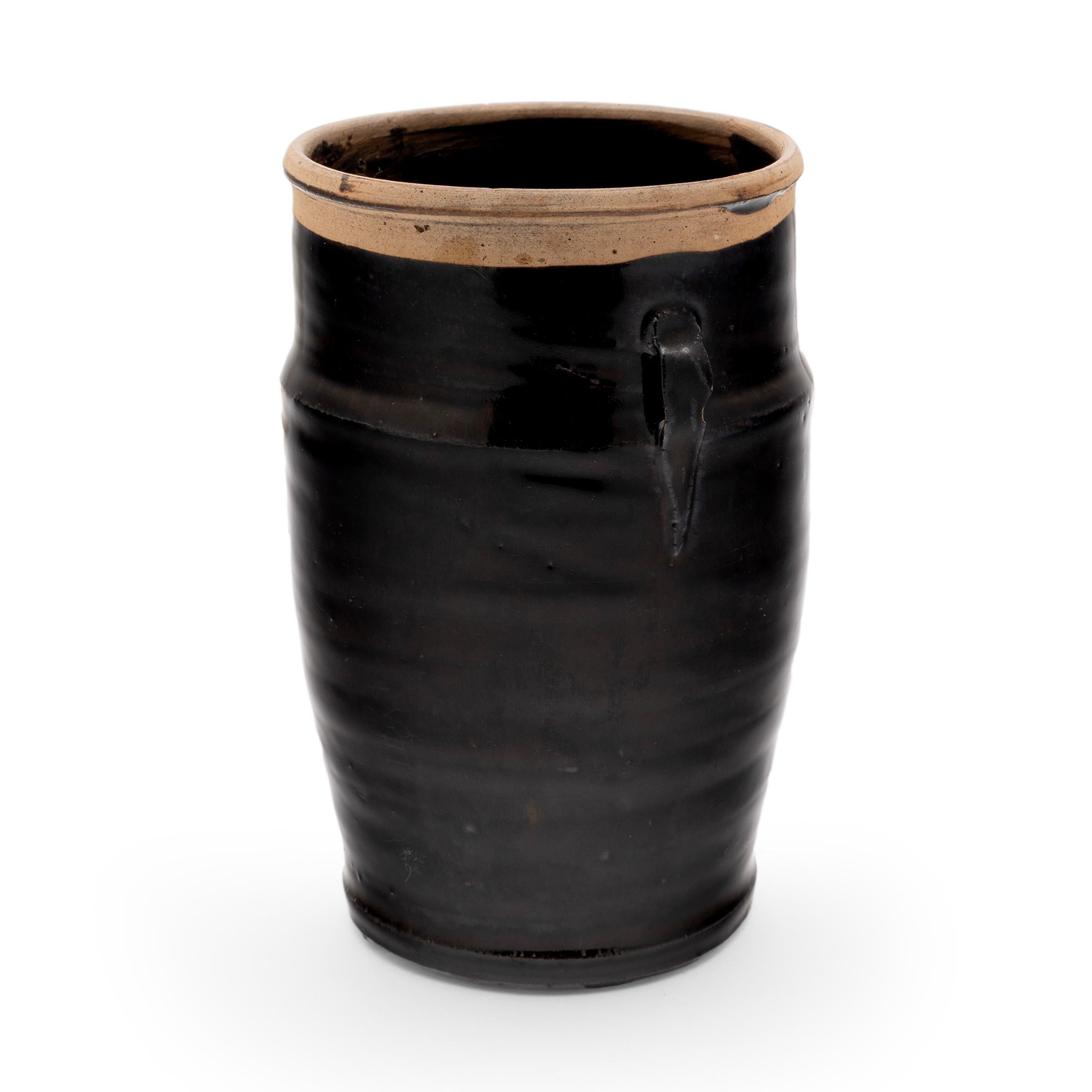 An opaque black glaze coats the body of this small early 20th-century kitchen jar. As evidenced by the glazed interior, the jar was once used daily in a Qing-dynasty kitchen for fermenting or storing foods and condiments. The wide-mouth jar has a