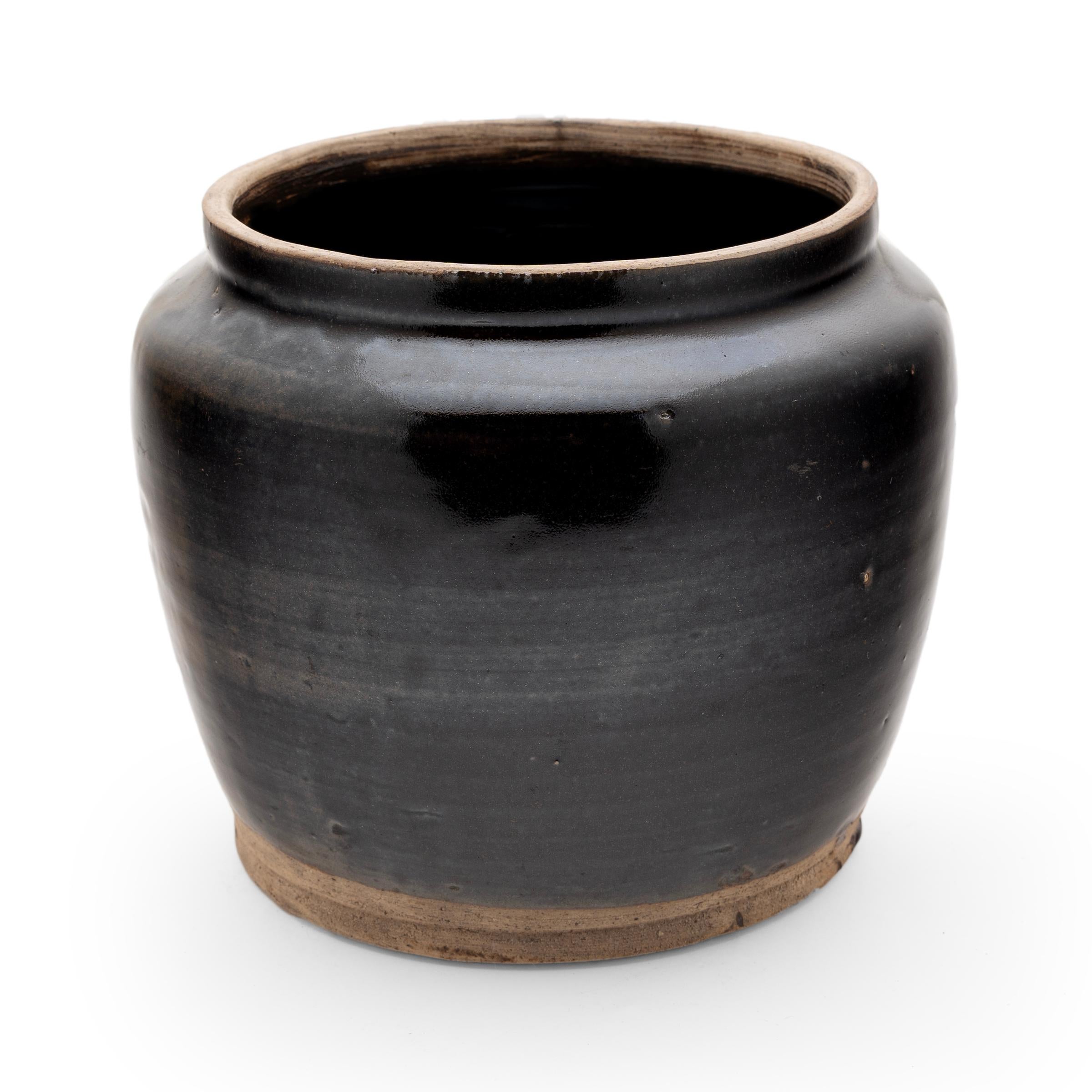 A glossy black glaze clings to the form of this small kitchen jar's banded surface. The glazed vessel dates to the early 20th-century and was used for storing food and condiments in a provincial Qing-dynasty kitchen, as evidenced by its interior