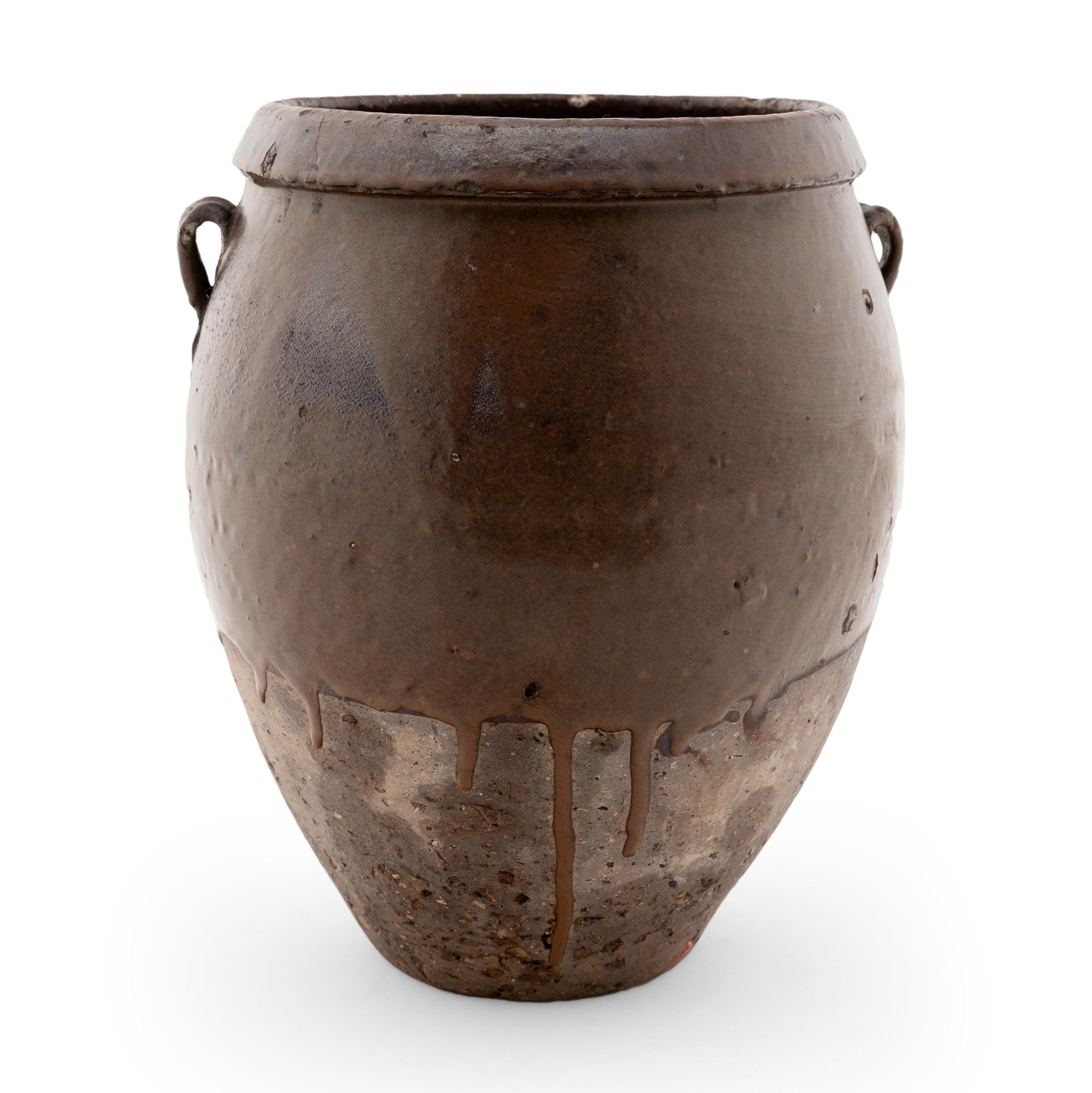 This early 20th-century vessel emulates the full-bodied shapes and unusual glazing found in ancient ceramics. A thick brown glaze clings to the upper half of the jar, dripping to a stop and leaving the lower half mostly unglazed. Some glaze seems to