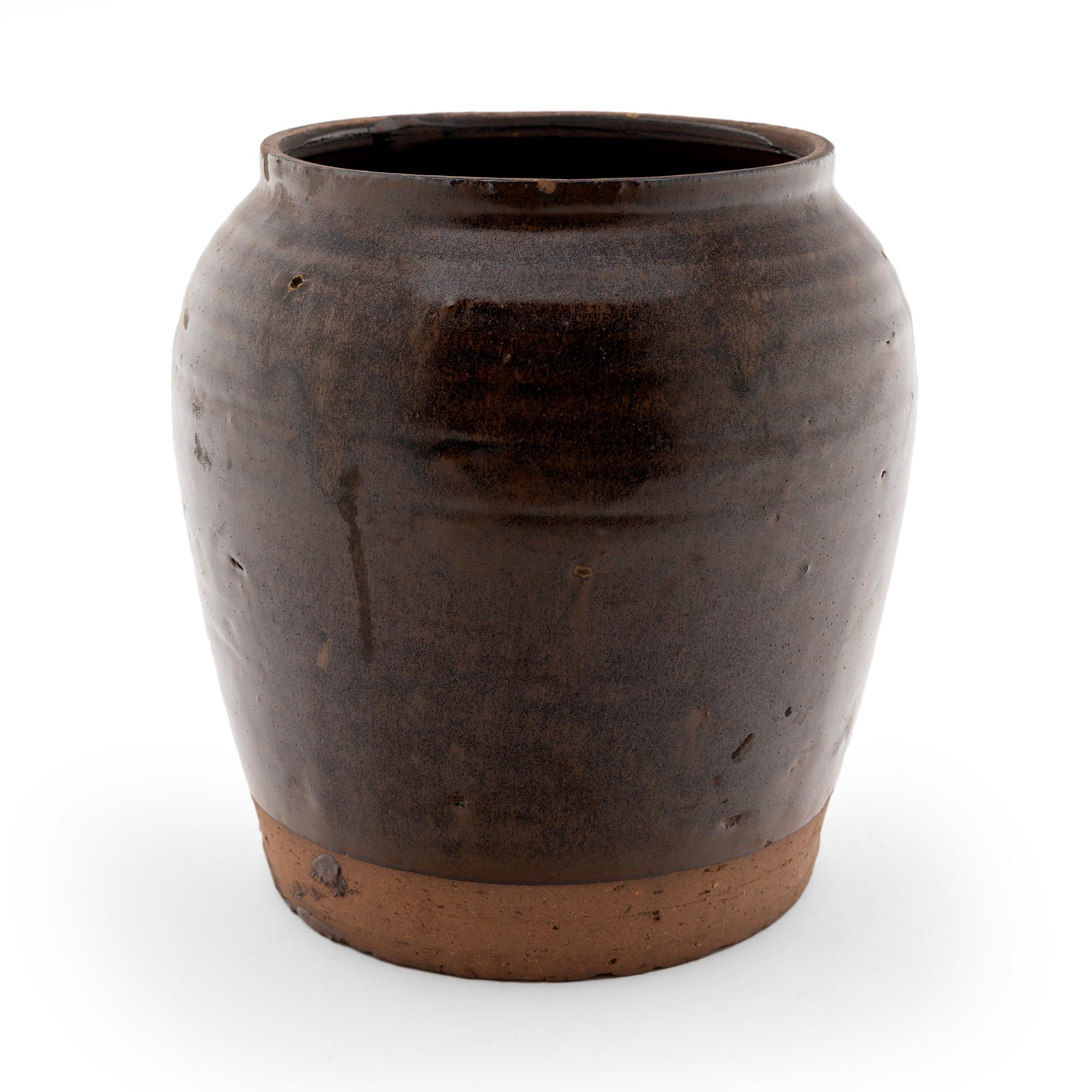 Cloaked inside and out with a dark brown glaze, this Chinese terra cotta kitchen jar dates to the early 20th-century. As evidenced by the glazed interior, this wide-mouth jar was used in a provincial Chinese kitchen for fermenting foods and