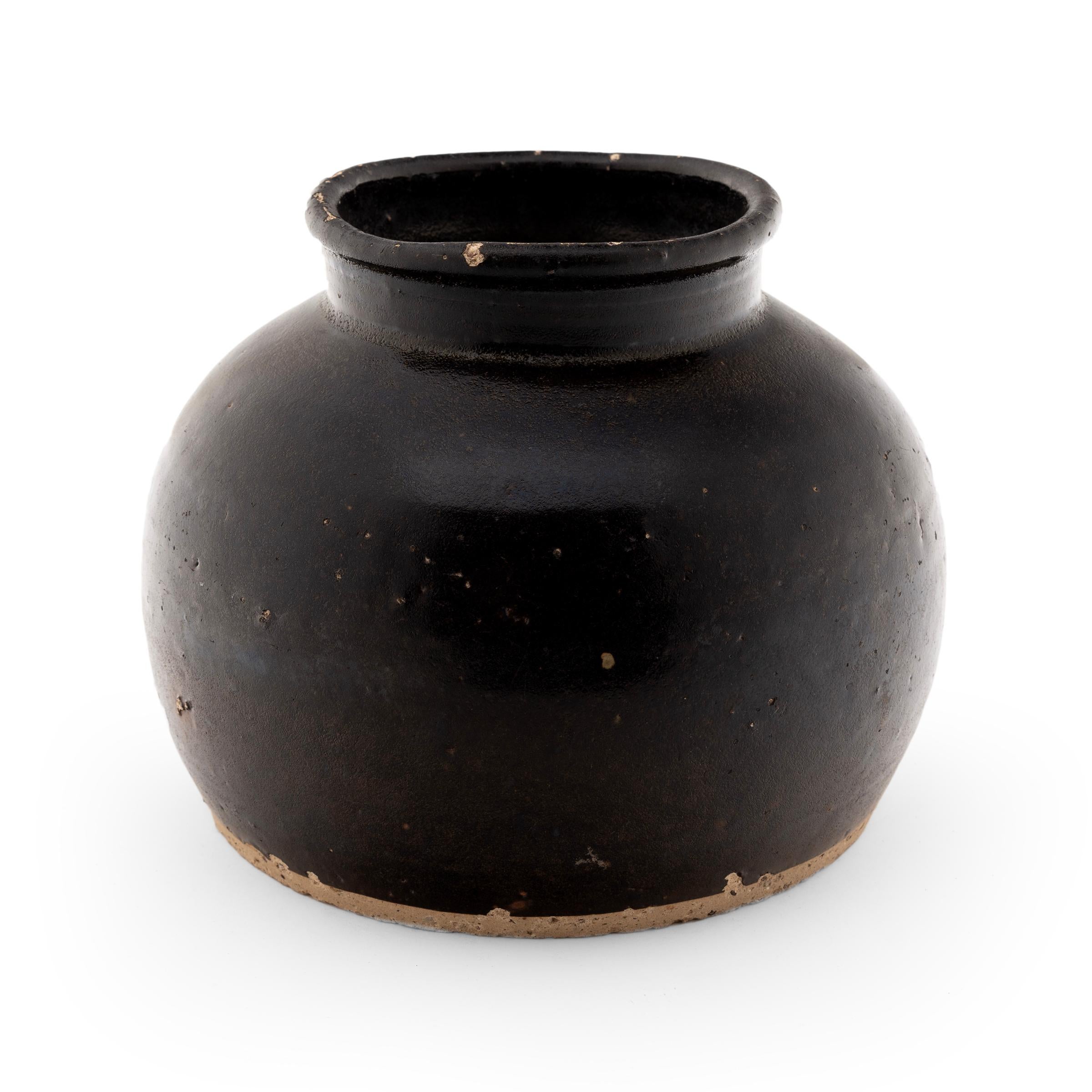 Crafted in the early 20th century, this small glazed jar was once used in a Qing-dynasty kitchen to store vinegar, wine or condiments, as evidenced by its narrow neck and interior glaze. In contrast to its unfinished base, the jar boasts a thick,
