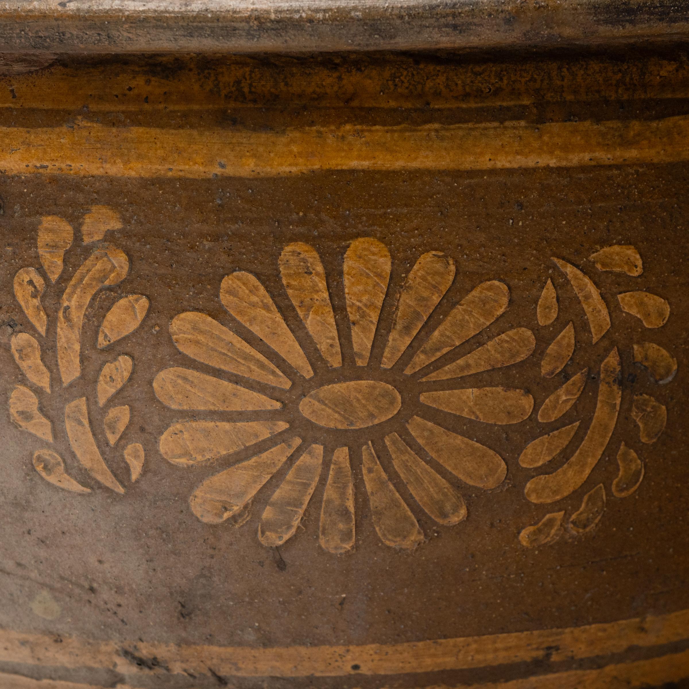 This low terracotta planter sits with a minimal form and a perfectly imperfect glazed finish. The vessel has a simple, tapered silhouette, shaped with a wide mouth, short walls and a flattened rim. A charming design of chrysanthemum blossoms