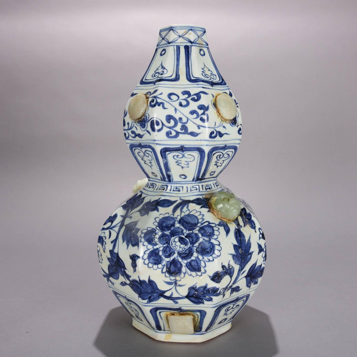 Chinese art pottery vase features gourd form with blue and white glazed foliate and floral decoration and applied jade carvings including masks, 20th century

Measures: 15