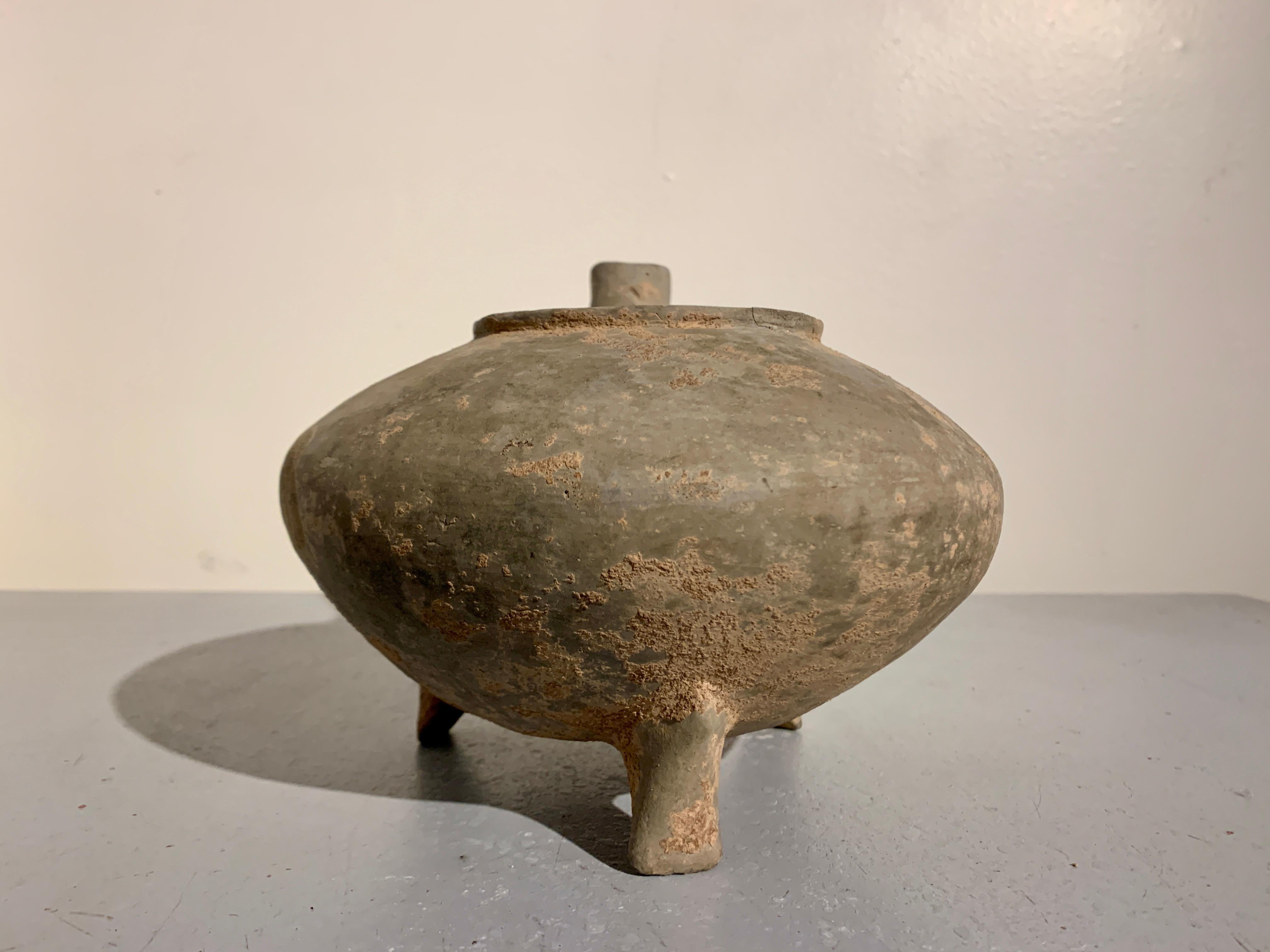 An unusual Chinese gray pottery pouring vessel, he, Warring States or early Han Dynasty, circa 4th - 3rd century BC, China.

The pouring vessel, called a he, is supported by triangular tripod feet. The compressed globular body with a wide opening