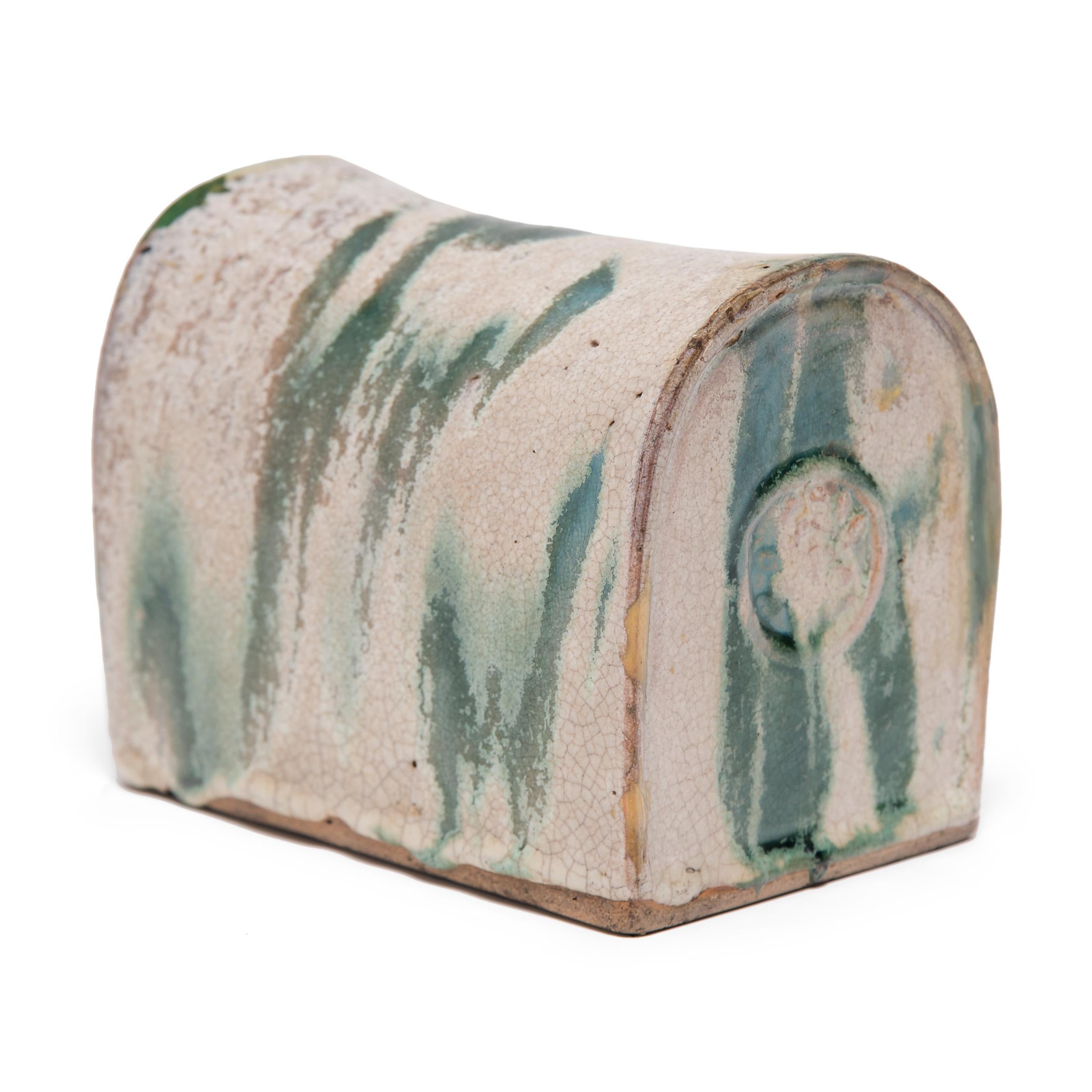 To keep her elaborate hairstyle intact while sleeping, a well-to-do woman once used this ceramic headrest as a pillow. Dating to the late Ming dynasty, this glazed headrest embodies the quiet simplicity of the era. A glassy blue-green glaze drips