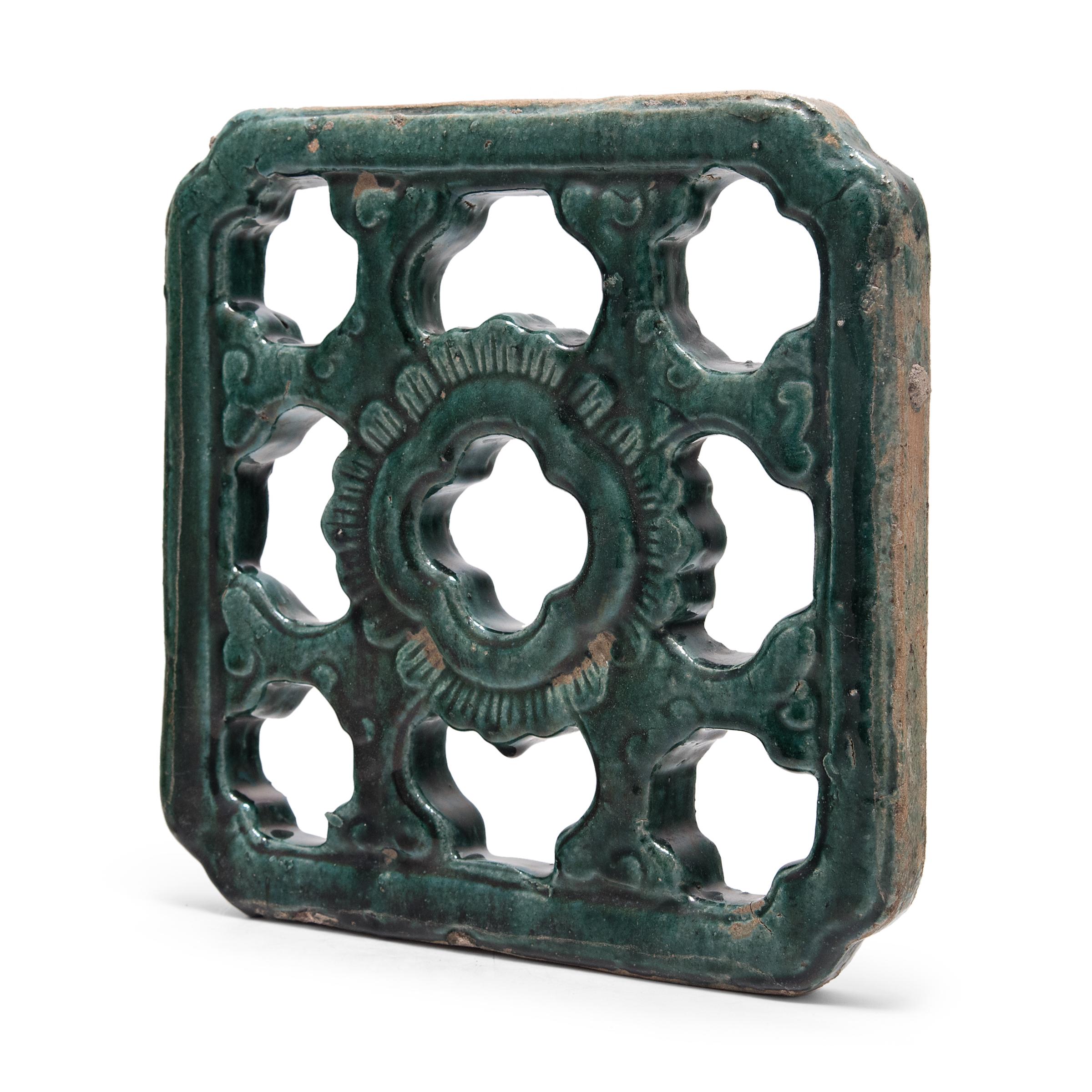 This early 20th century breezeway tile has a simple lattice design comprised of swirling clouds around a central floral motif. A beautiful turquoise-green glaze cloaks the exterior, pooling in every crevice with dark, richly saturated color. Much