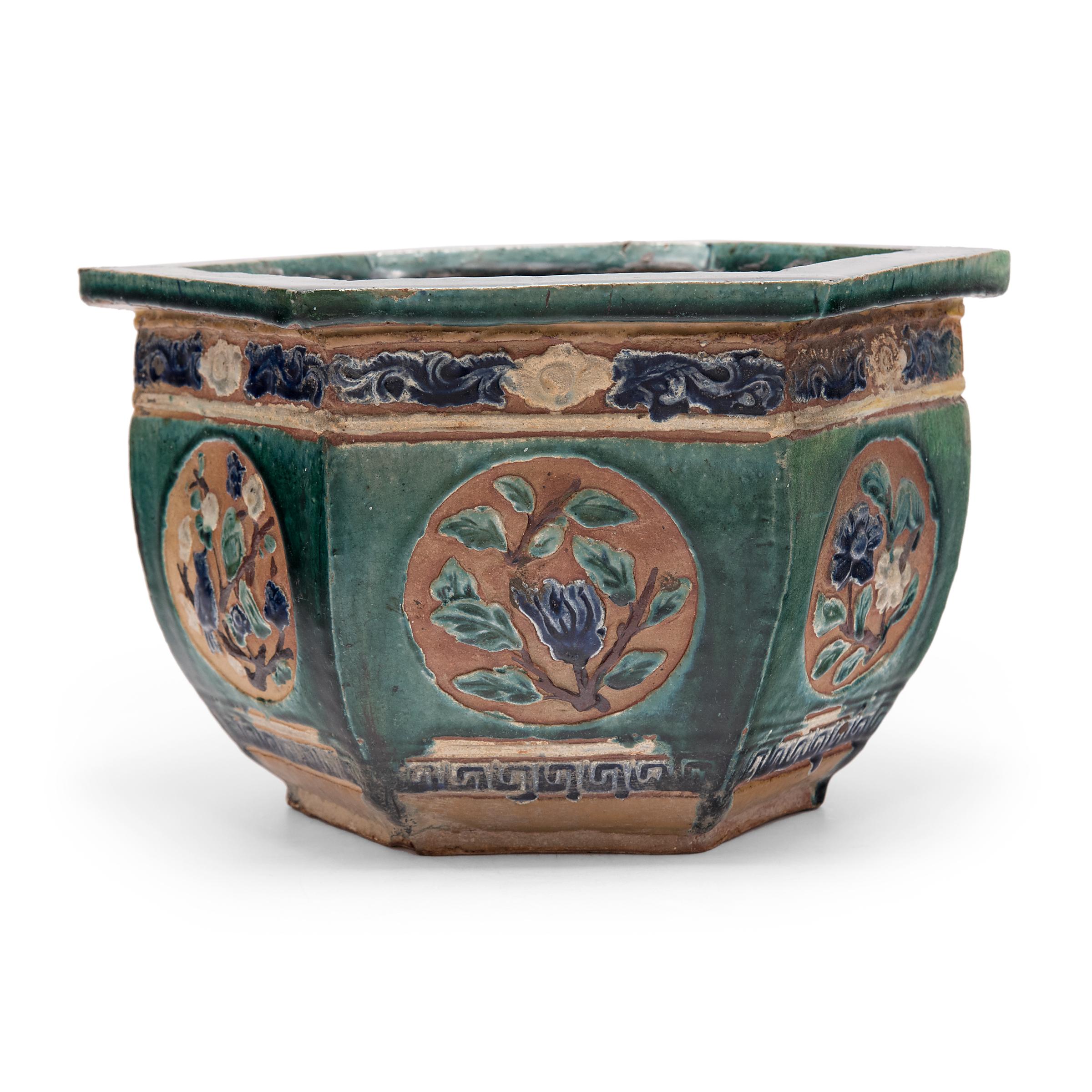 This low ceramic planter dates to the early 20th century and features a wide opening, flat rim, and six gently curving sides. The basin is patterned in low relief with bands of scrollwork and round medallions of flowers, birds, and offering fruits.