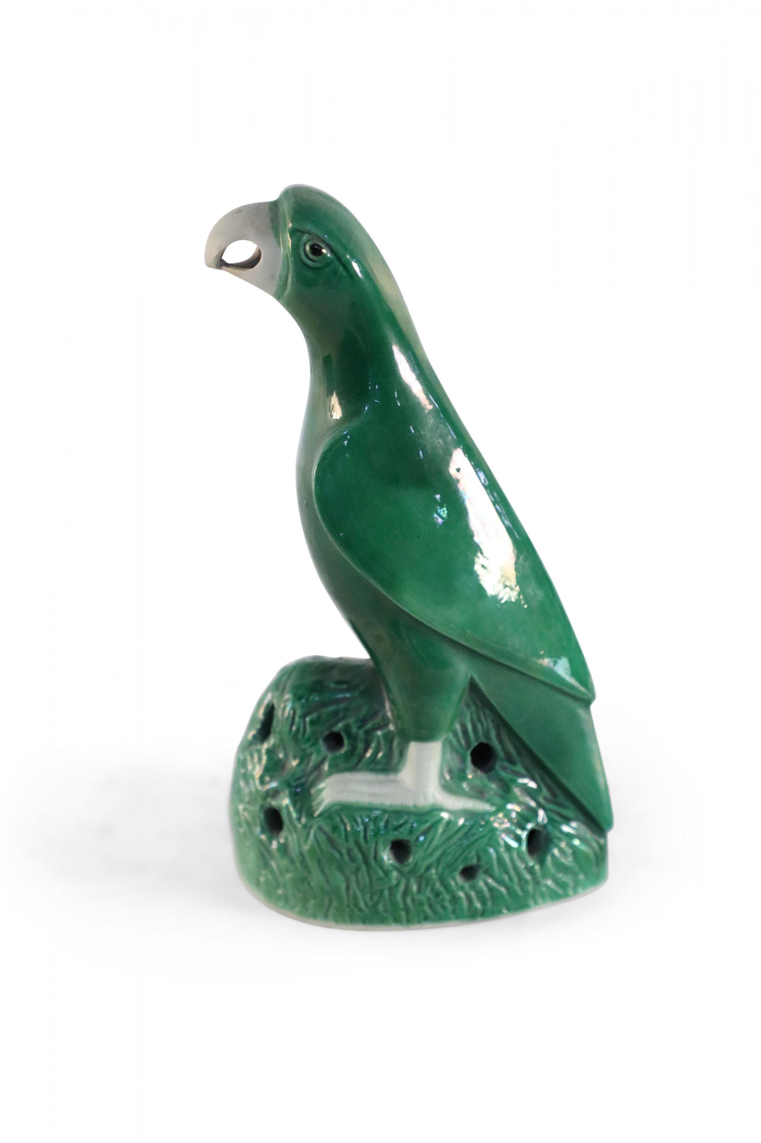 Vintage Chinese glazed porcelain statue of a green parrot with a gray beak and talons perched atop matching green grasses.
 