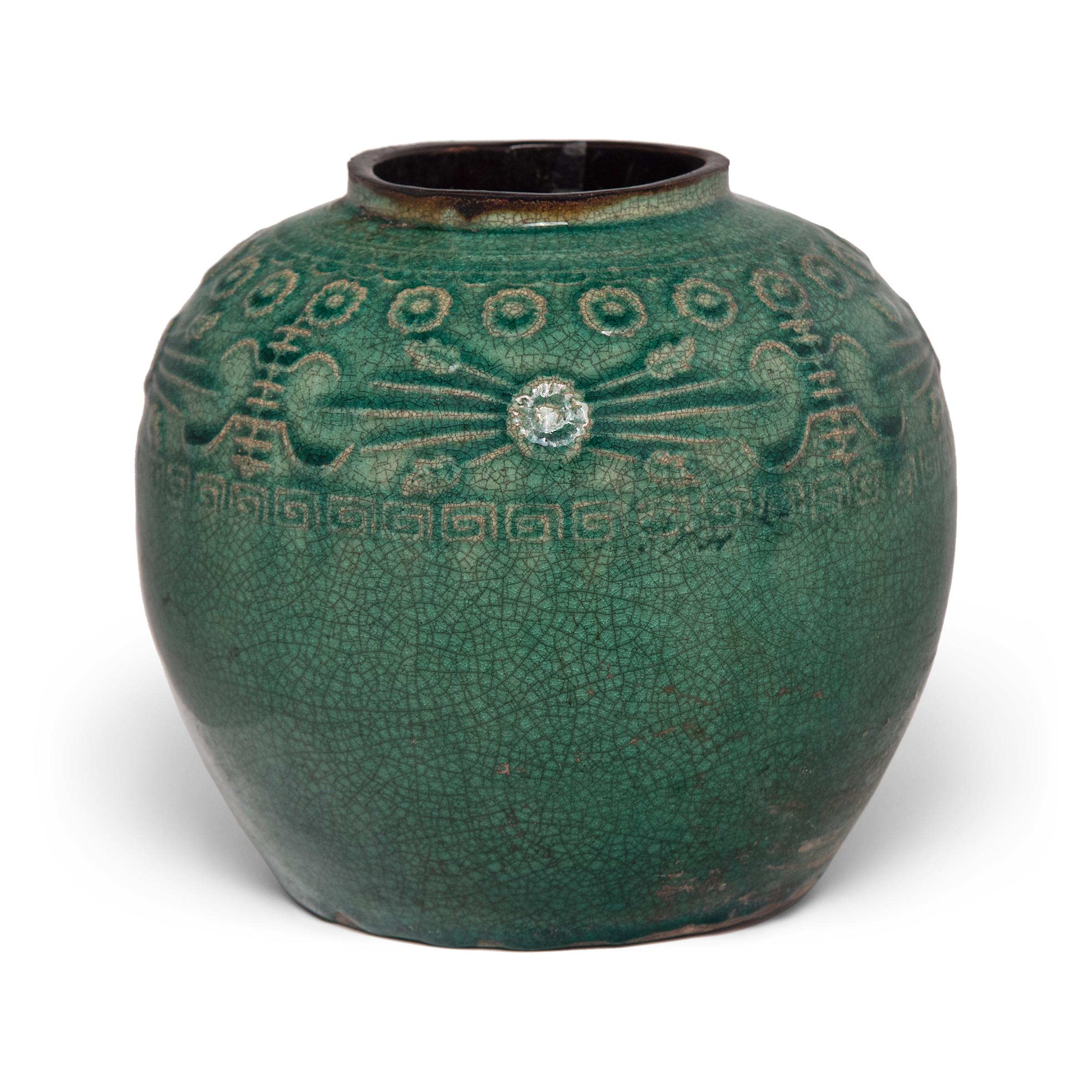 A glassy blue-green glaze sheets, pools, and drips across the rounded body of this provincial kitchen pot, lingering beautifully on the low relief decoration to the jar's shoulders. Among these raised patterns are chrysanthemum blossoms for