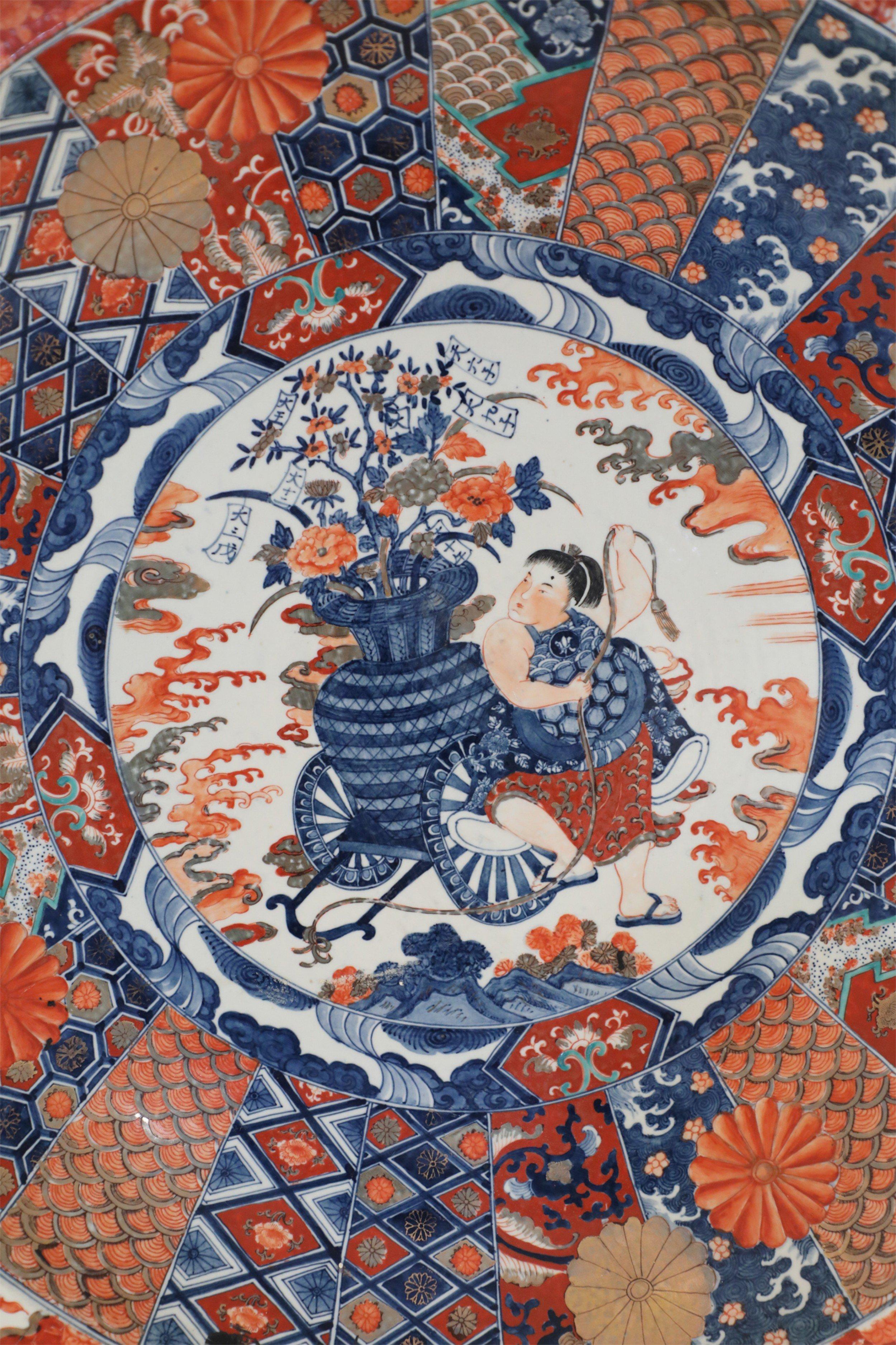 Antica ciotola da centrotavola in porcellana cinese Guangcai (fine del XIX secolo) decorata con pannelli a motivi blu e arancioni intorno a una scena centrale di una donna che cammina con una grande urna piena di fiori su un carro e fiori arancioni