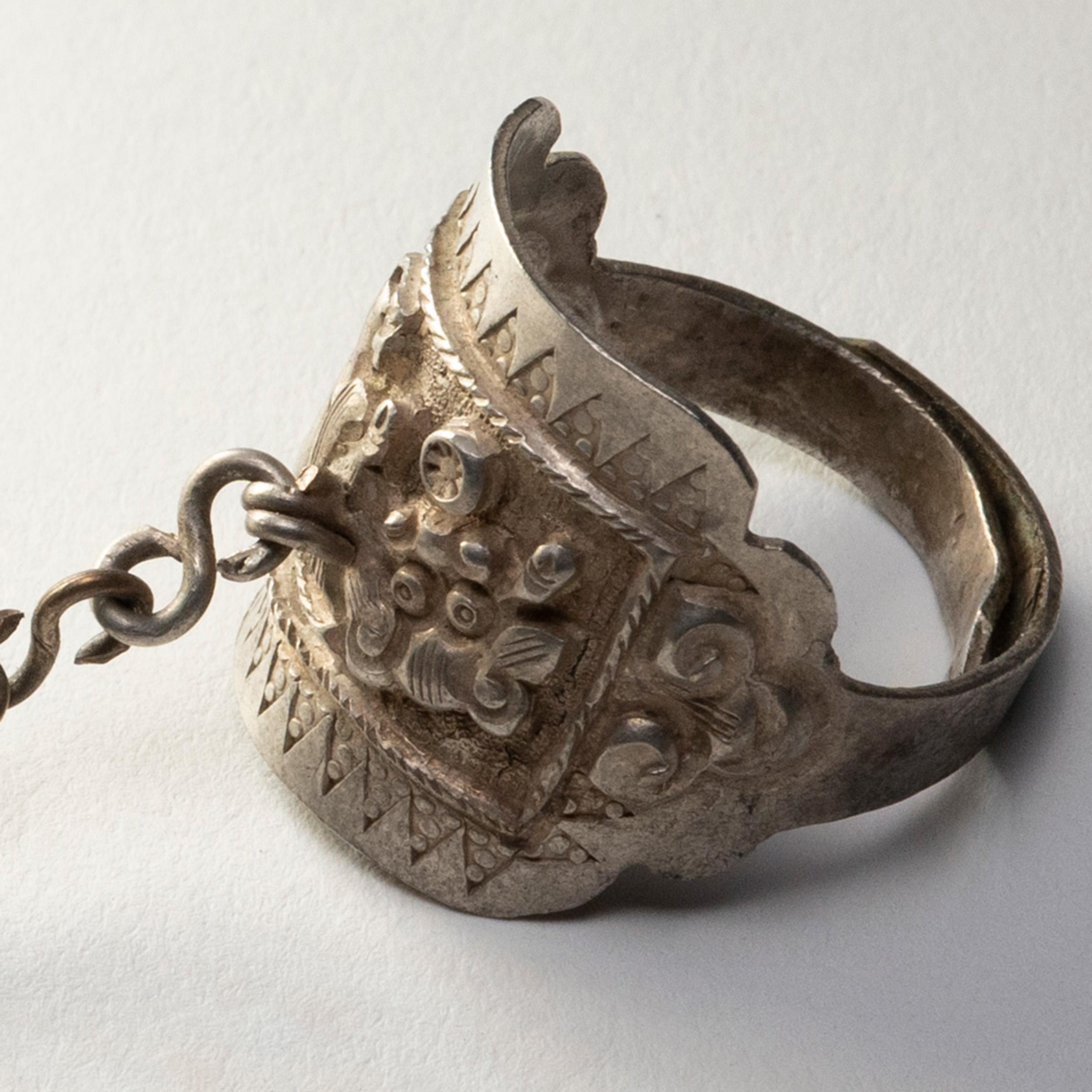 Dated to the late 19th century, this silver charm ring was believed to protect the wearer from bad luck and malevolent spirits. The ring is decorated in relief with a repoussé design of a reclining fu lion, enclosed by a geometric border and flanked