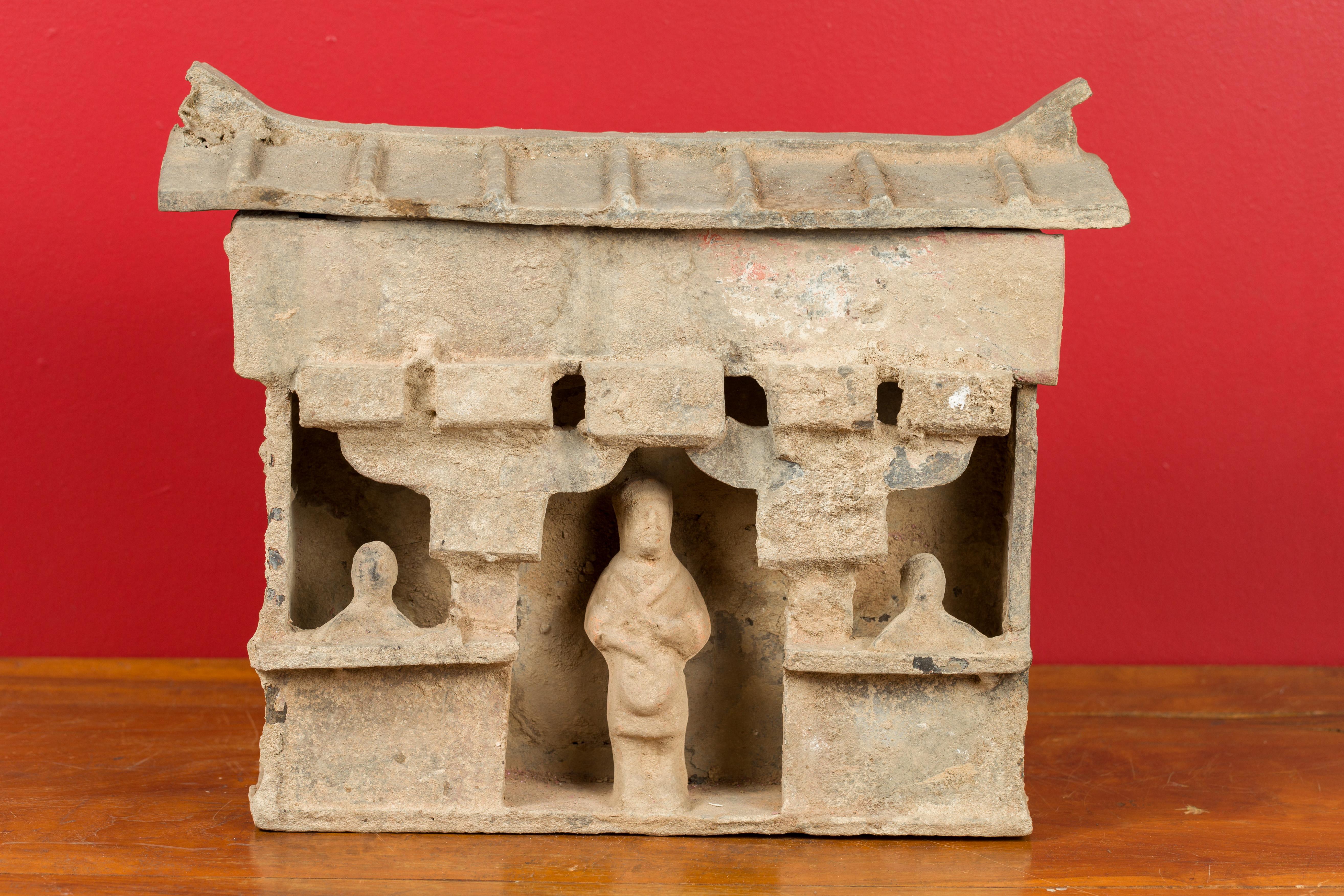 A Chinese Han dynasty house model with its occupants and removable roof, circa 202 BC-200 AD. Crafted during the Han dynasty, this mingqi house model features a removable roof sitting above an open room. Standing in front of each opening (a central