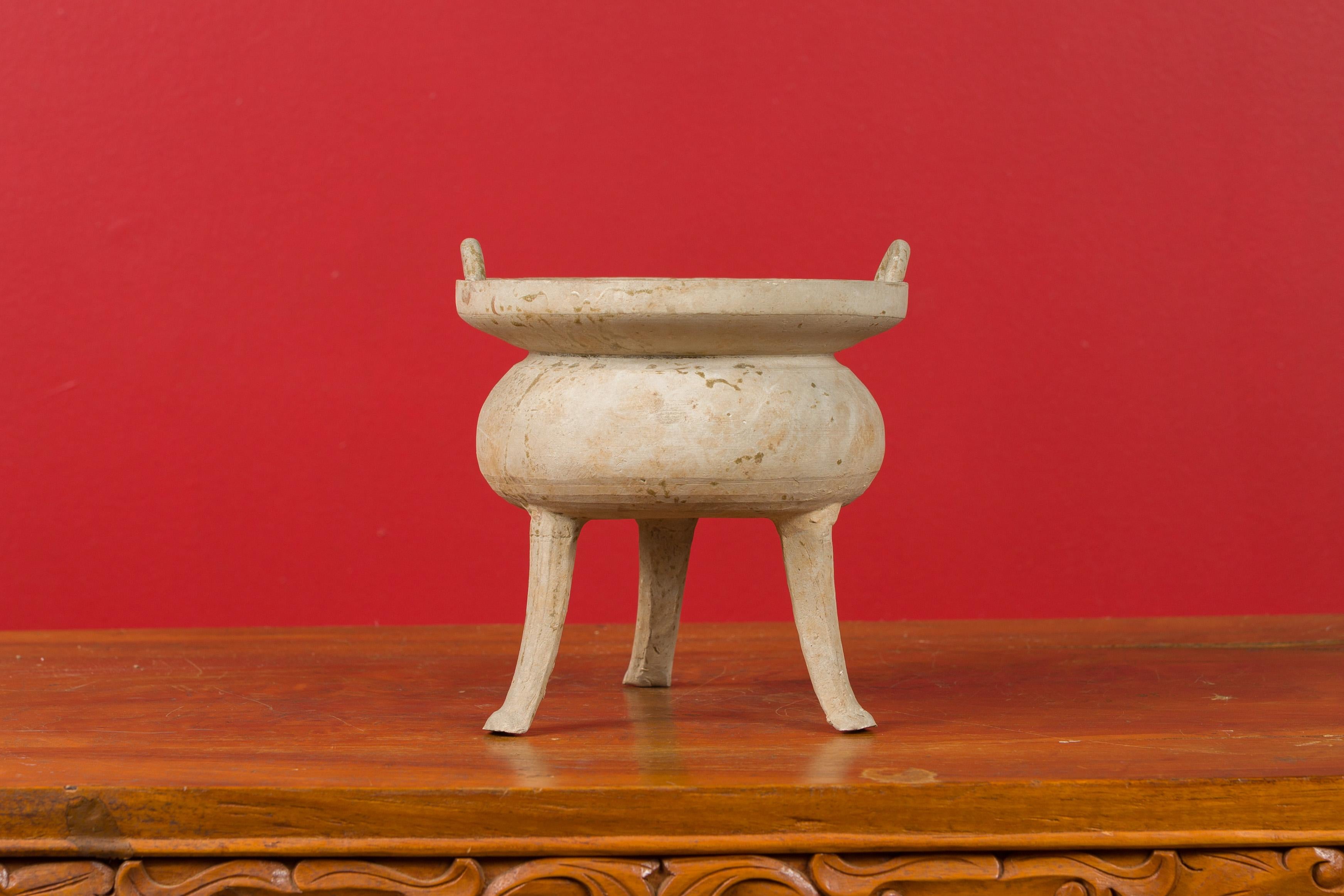 A Chinese Han dynasty period incense burner circa 202 BC-200 AD, with petite lateral handles and tripod base. Created in China during the prestigious Han dynasty, this ancient incense burner features a circular shape topped with petite handles, the