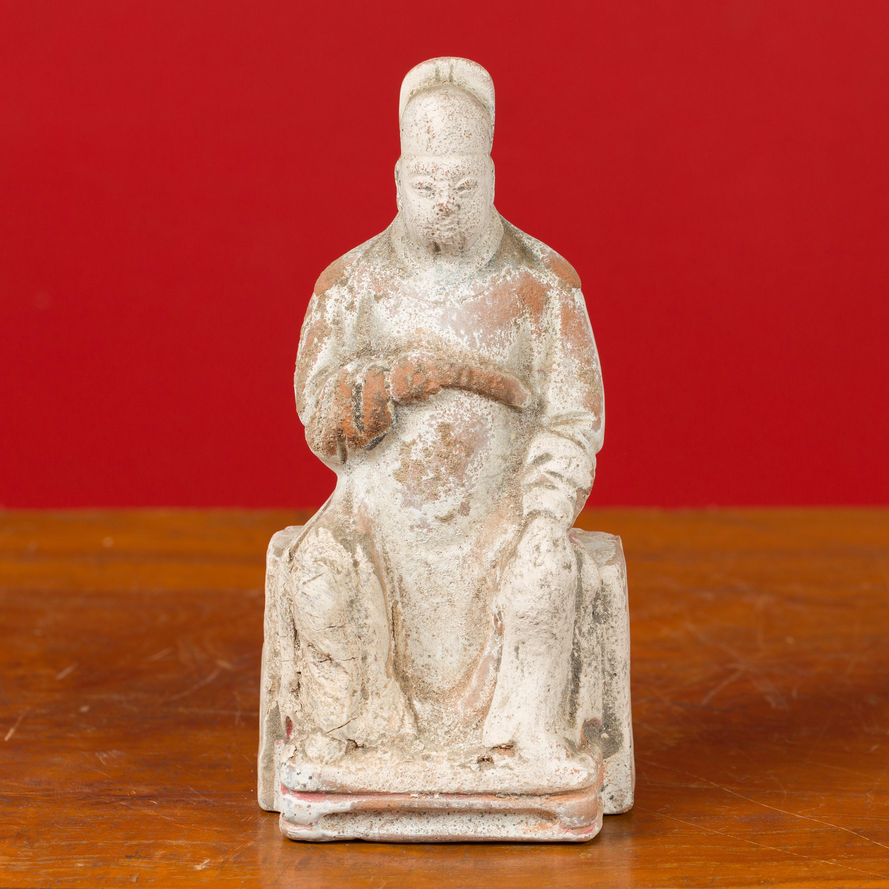 A Chinese Han dynasty period dignitary figure with original pigmentation, circa 202 BC-200 AD. Created in China during the prestigious Han dynasty, this small terracotta sculpture features a courtsman sitting in a stately manner on a pedestal.