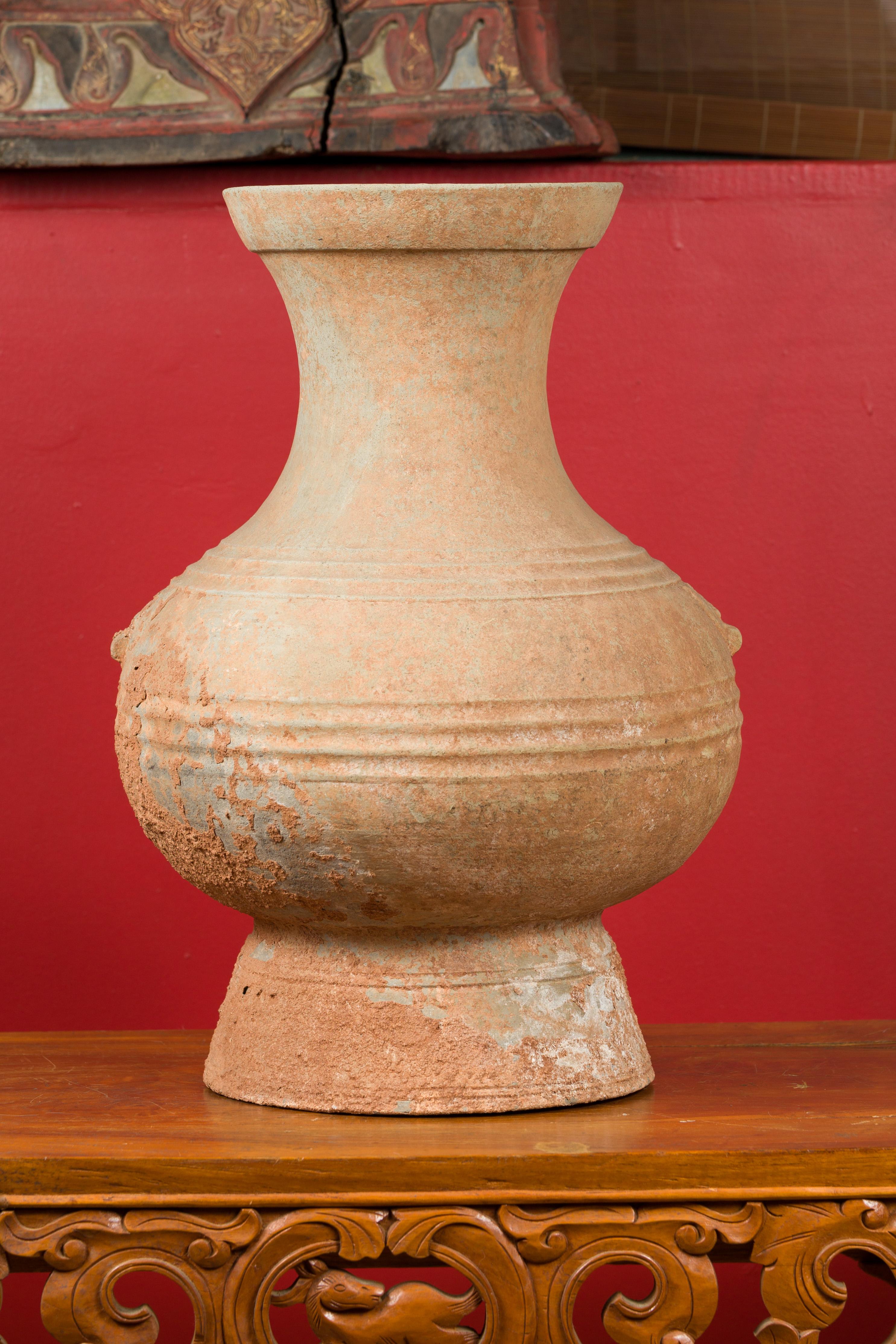 A Chinese Han dynasty period unglazed terracotta Hu vessel circa 202 BC-200 AD, with incised decor, mineral deposits and lateral accents. Crafted in China during the Han dynasty, this terracotta wine vessel, called a Hu vessel, features a generous