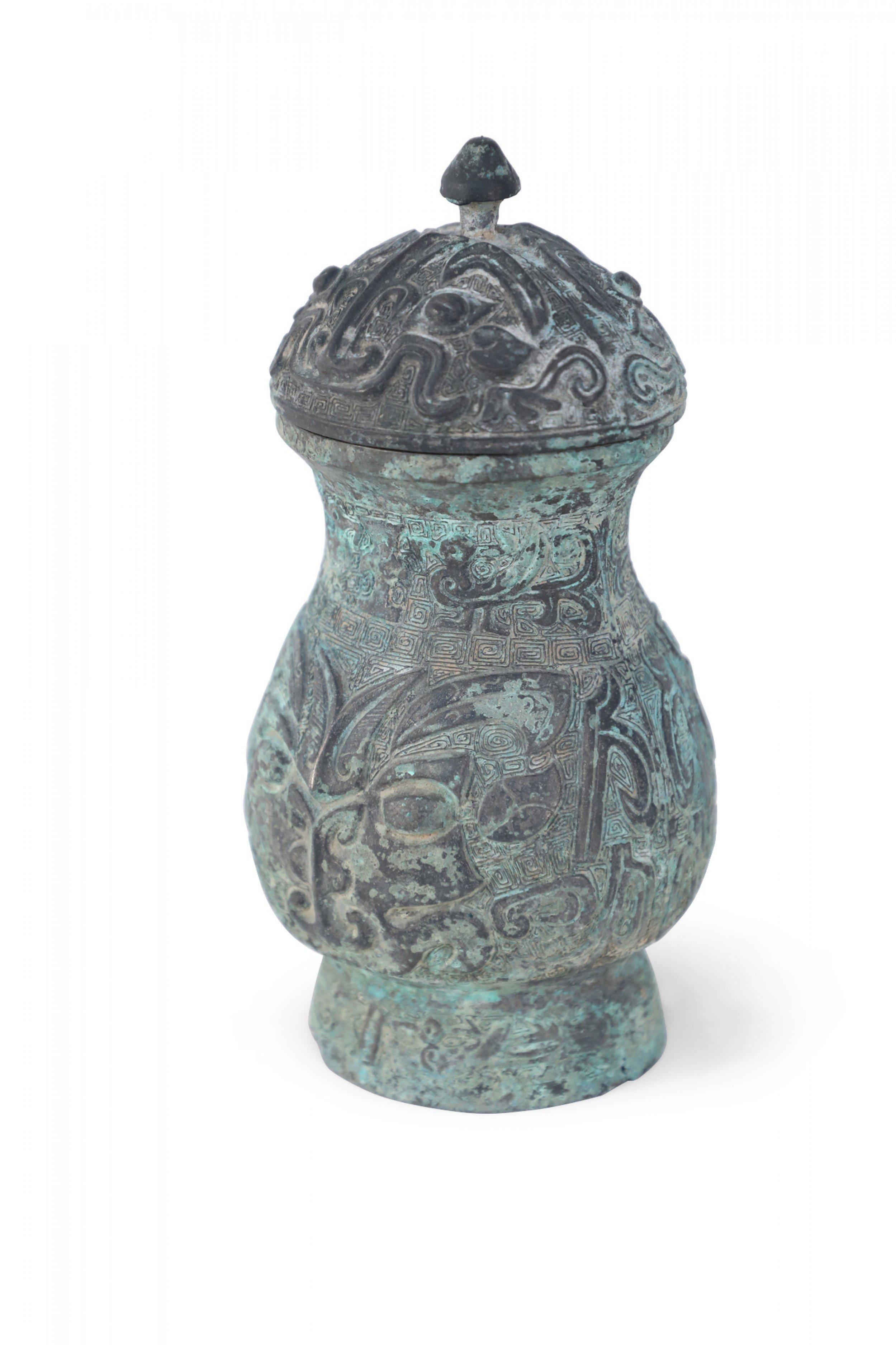 Copie ancienne d'une jarre à couvercle en bronze de la dynastie chinoise des Han, décorée des hauts et des bas de sa patine verte, sculptée de motifs géométriques en relief et surmontée d'un couvercle en forme de dôme et de fleuron.