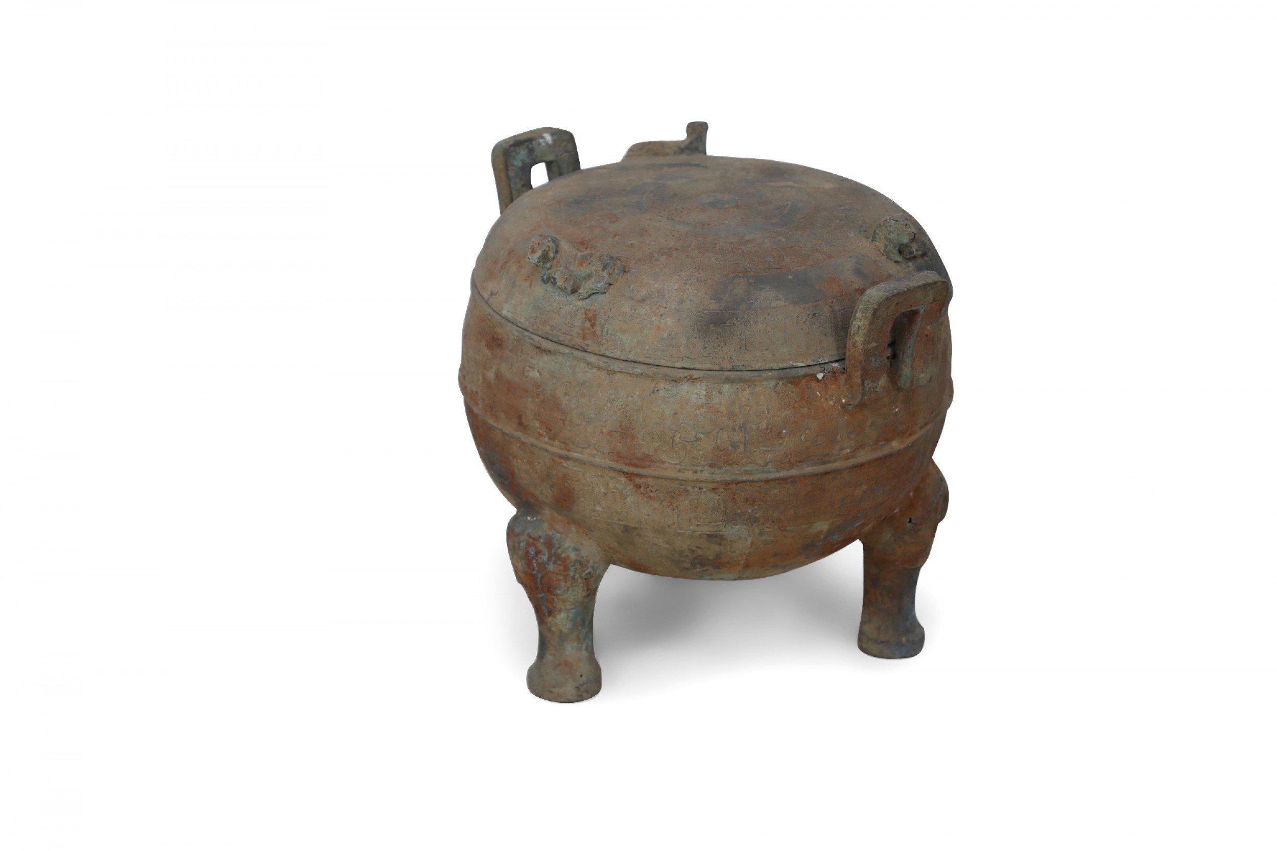 Antique Chinese Han Dynasty-style copy of a patinated bronze lidded pot etched with a subtle, all-over geometric pattern, sitting atop three feet, fitted with two handles and topped with a lid bearing three cow figurines.

Condition: Good; Wear