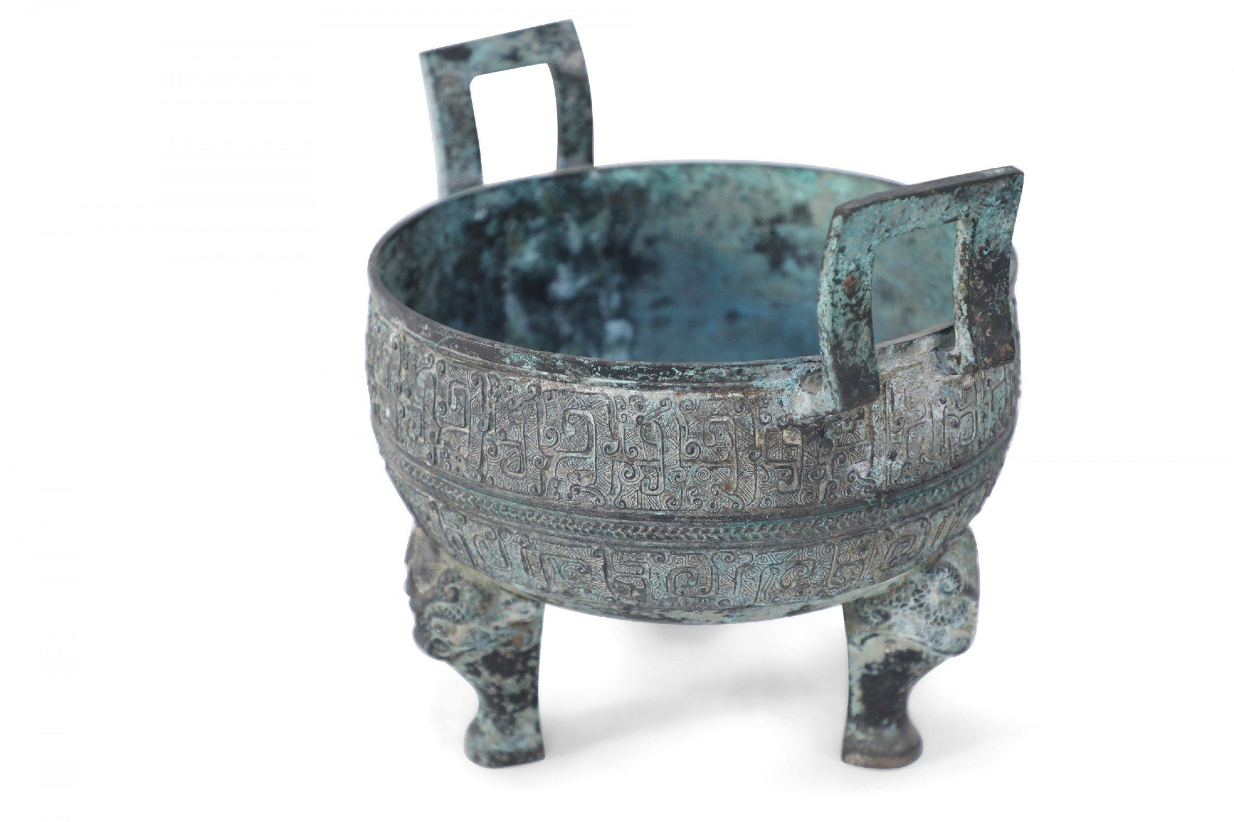 Antica copia in stile Dinastia Han cinese di un vaso in bronzo patinato scolpito con bande geometriche in rilievo che ne avvolgono la forma, seduto in cima a tre zampe di leone e dotato di due manici verticali quadrati.