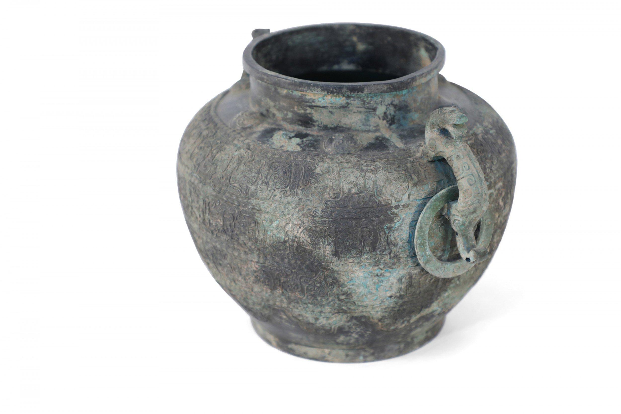 Antique Chinese Han Dynasty-style copy of a patinated bronze pot decorated with intricate raised pattern banding wrapping its form, two serpentine handles with hanging rings and a gray patina.
