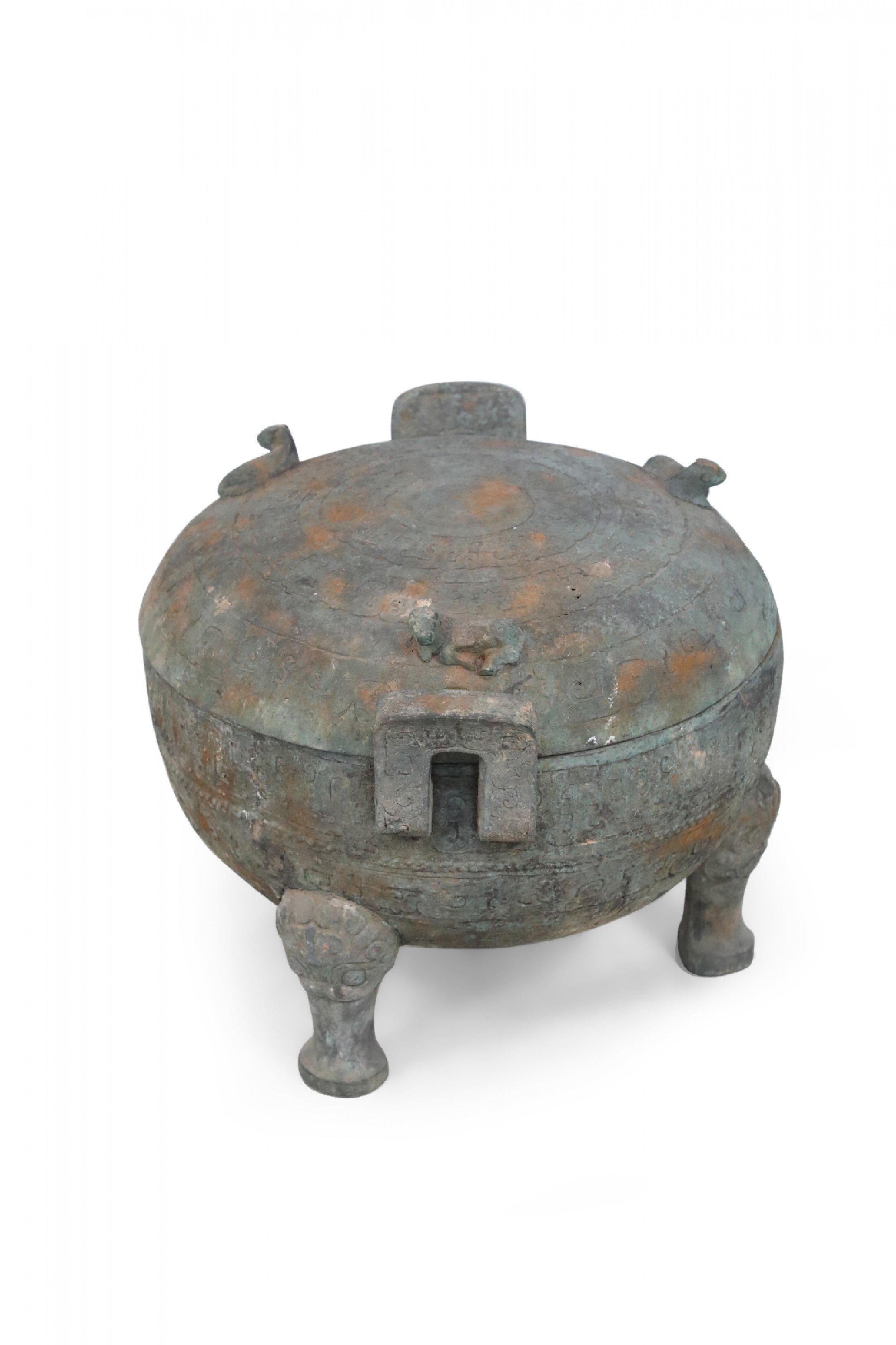 Antique Chinese Han Dynasty-style copy of a patinated bronze pot etched with raised geometric patterned bands wrapping its form, sitting atop three feet, fitted with two handles and topped with a lid bearing three cow figurines.

Condition: Good;
