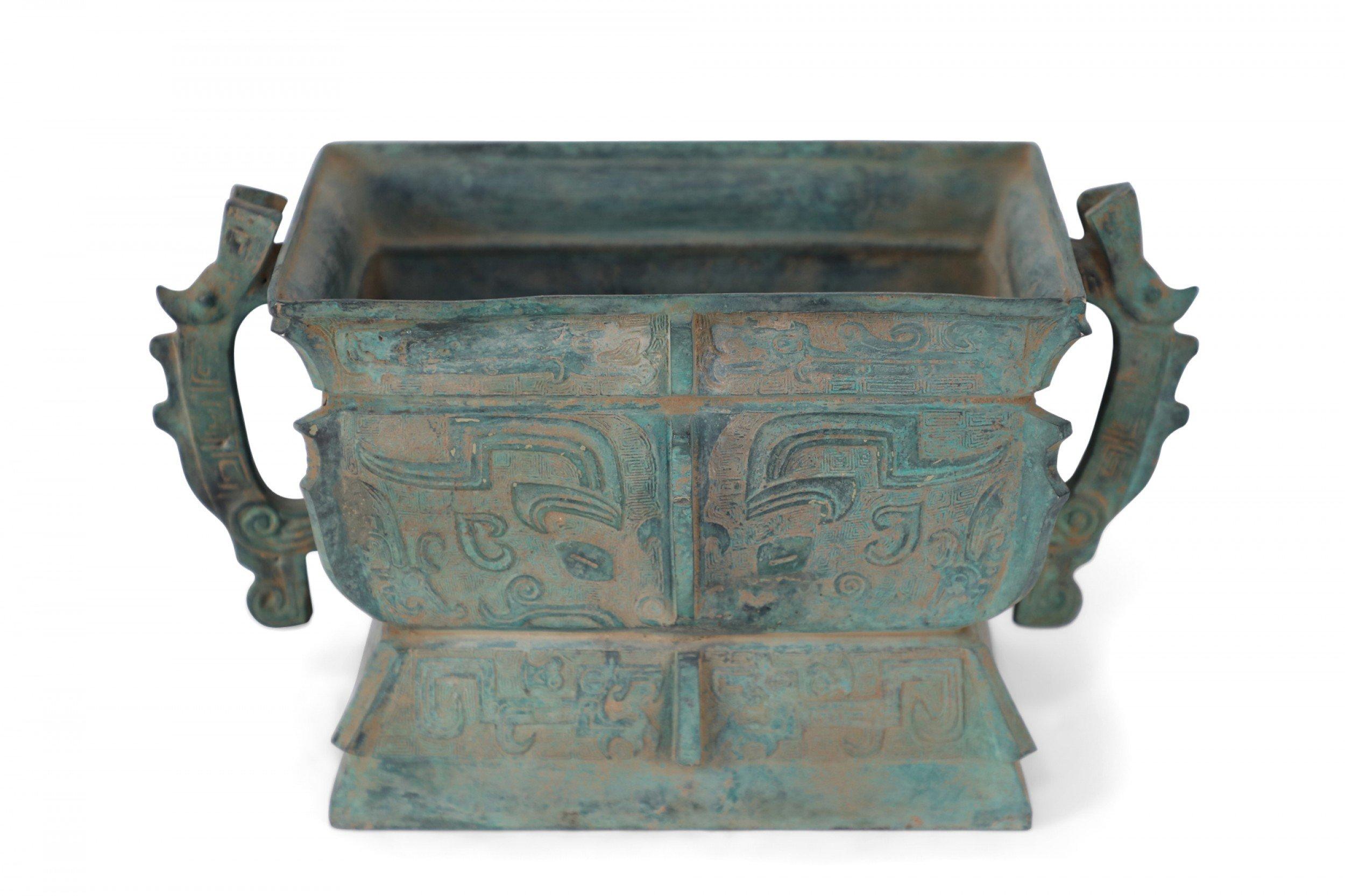 Antique Chinese Han Dynasty-style copy of a bronze tapered urn with a green patina, decorated with raised geometric patterns, accented with two handles and sitting atop a trapezoidal foot.