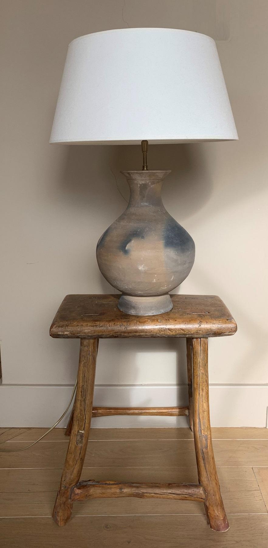 A table lamp made from a Han style Chinese vase with linnen hood. The vase probably 19th century in grey earthenware with darkgrey ashmarks. These marks are made by chance in the kiln and are experienced as a minimalistic decoration buy Asian