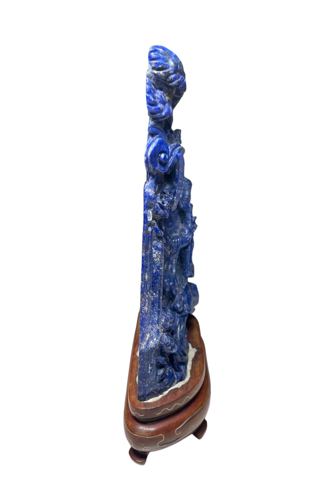 This is a hand carved small Chinese Lapis lazuli sculptures of the Guan Yin and the Phoenix bird over a wood trunk. Both sculptures are supported by a carved wood oval base.