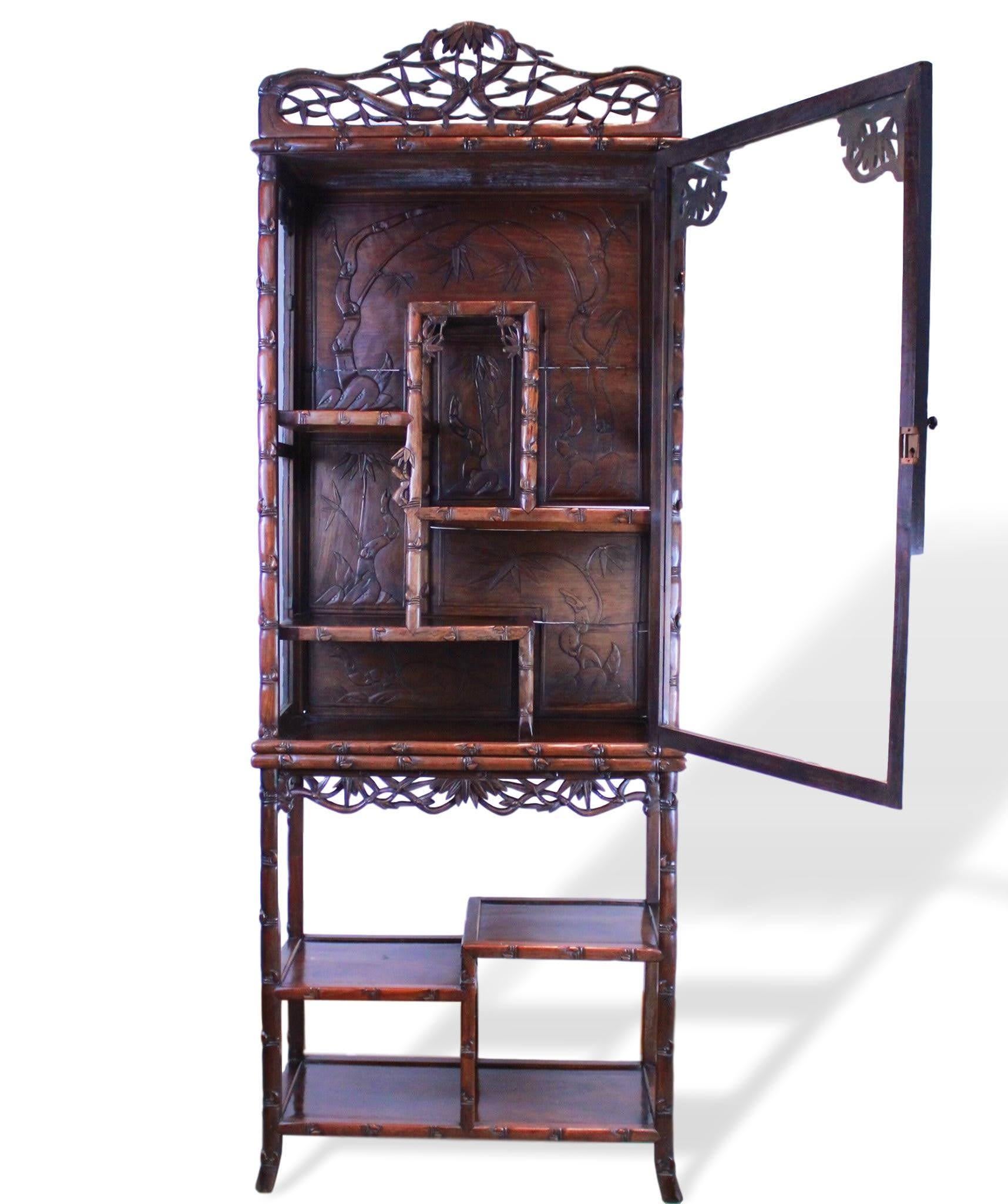 Chinese hand carved exotic rosewood display cabinet, circa 1880, carved throughout with simulated bamboo, with a single glazed door enclosing solid, irregular shelving trimed with further bamboo stalks and shoots, the solid wood back carved with