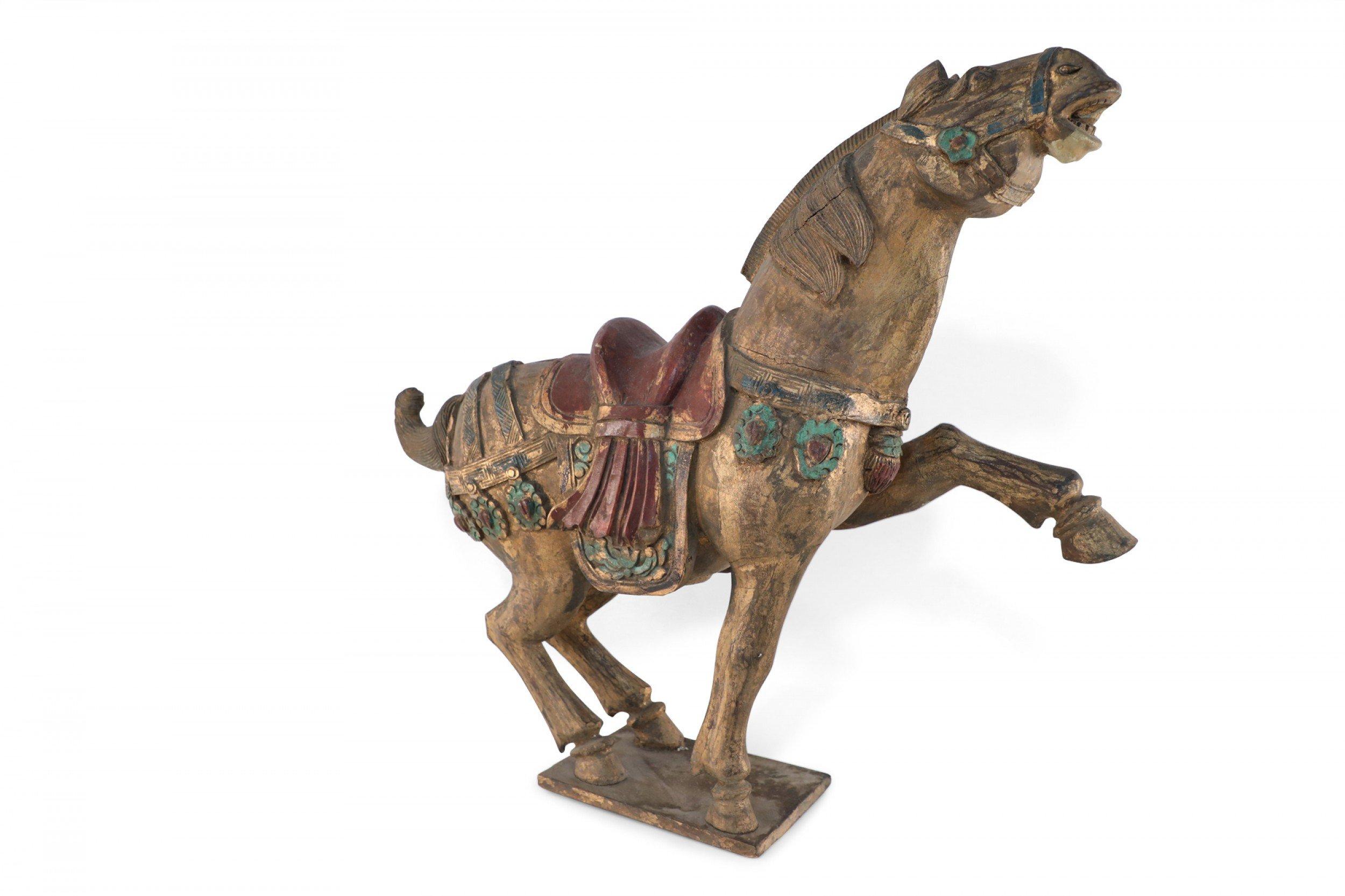 Chinese hand-carved wooden horse statue detailed with a saddle and decorative straps and painted in touches of metallic, red and green.
 