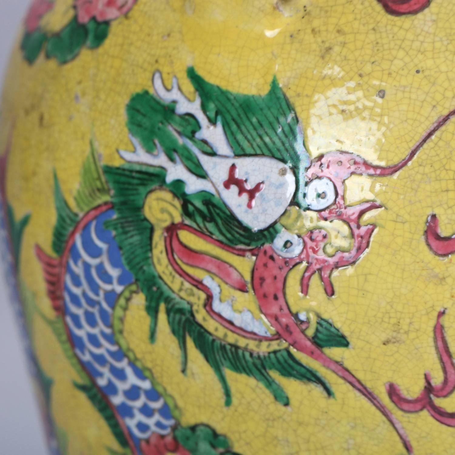 Chinese hand enameled art pottery lidded urn features wrap around Chinese dragon in setting of sky with clouds and over the sea on gold yellow ground and having four applied handles and lid, 20th century

Measures: 16