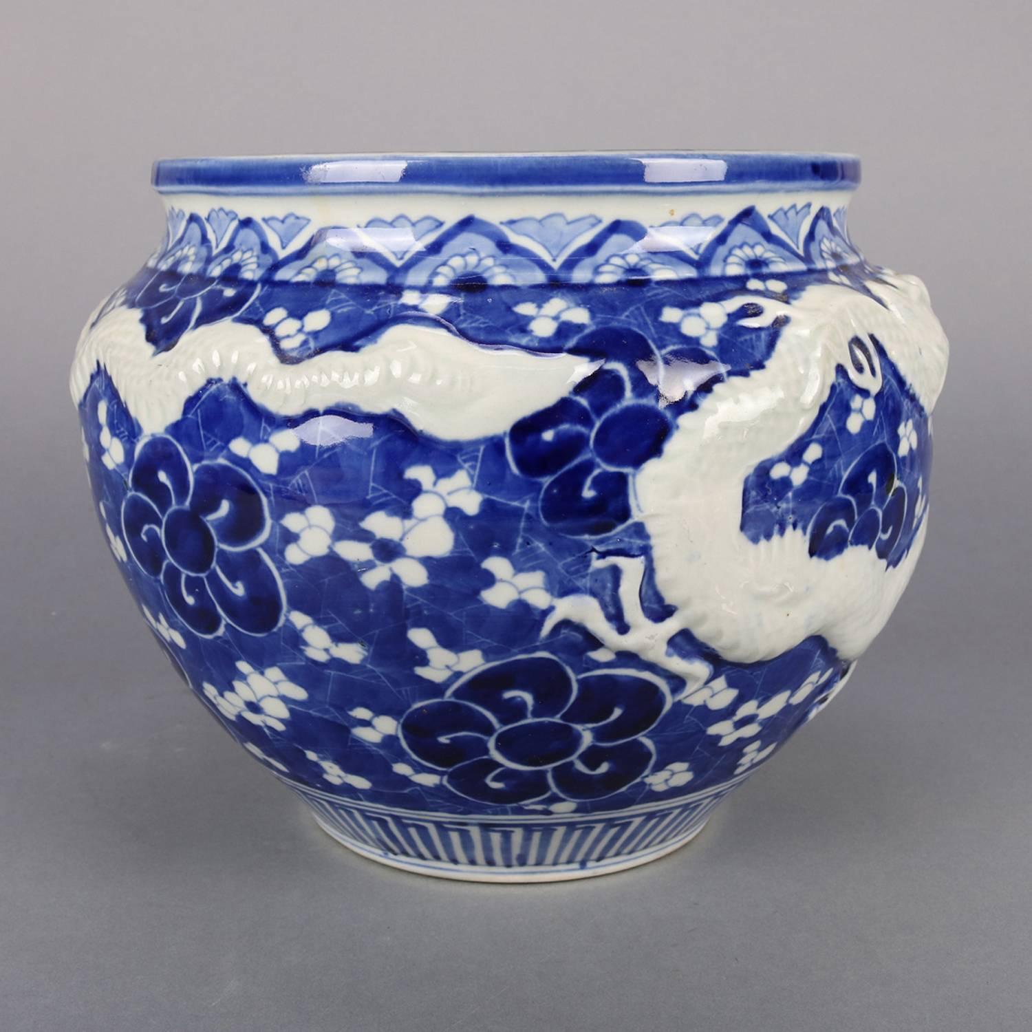 Chinese porcelain jardeniere features high relief dragon, hand painted allover floral decoration, collar with stylized tobacco leaf design, blue and white, 20th century

***DELIVERY NOTICE – Due to COVID-19 we are employing NO-CONTACT PRACTICES in
