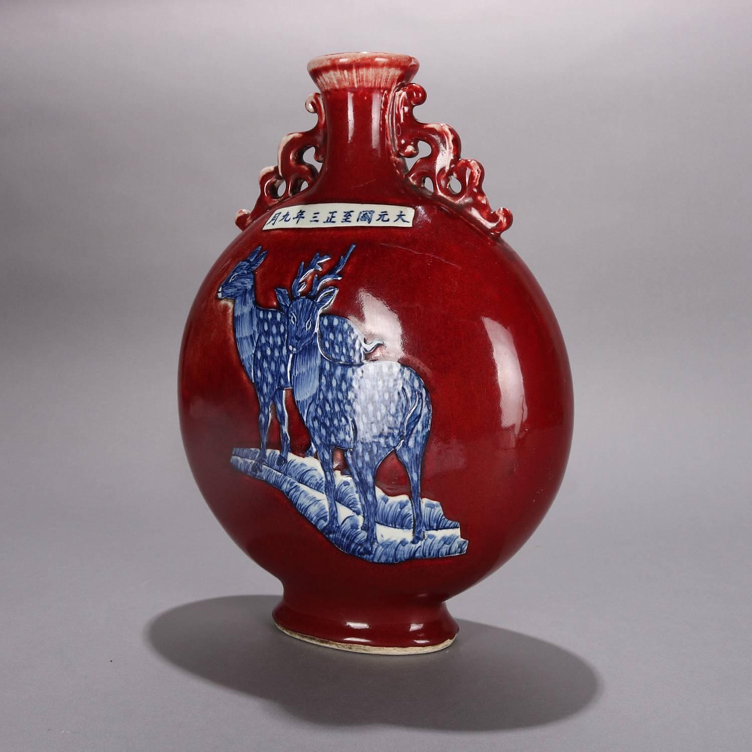 Chinese hand-painted flask vase features moon form with oxblood red glazing, double scrolled handles and central reserve with deer with chope mark titling above, 20th century

Measures: 14.25