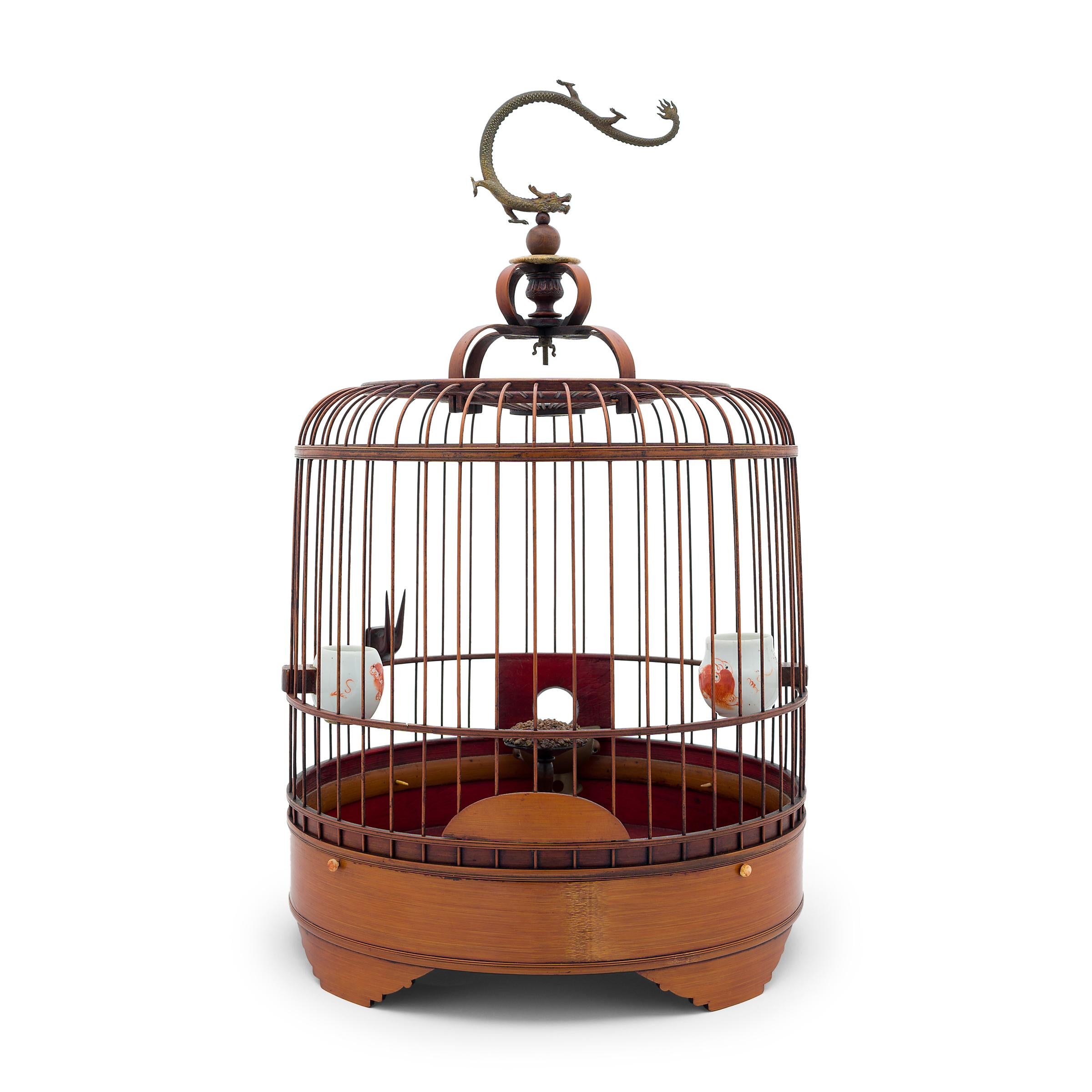This large, barrel-form birdcage dates to the early 20th century and is carefully assembled of thin bamboo rods fitted to a round bamboo base. The cage hangs from a large hook attached to the top, finely cast in the shape of a sinuous dragon. A