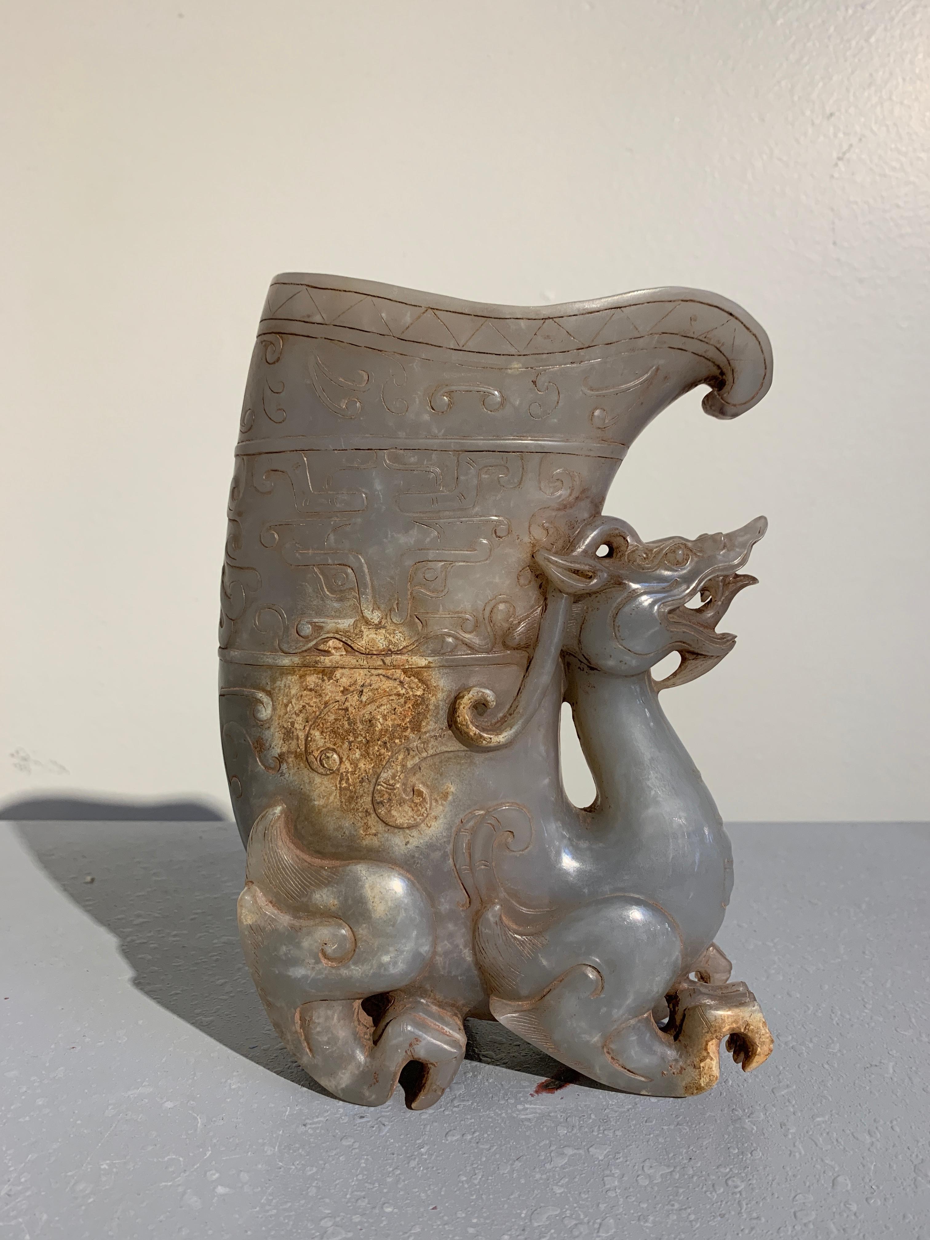 An early 20th century Chinese Republic period carved hardstone drinking vessel, called a rhyton, in the form of a mythical pixiu. 

The archaistic vessel carved in the Han Dynasty style from a single block of lavender gray nephrite and featuring a