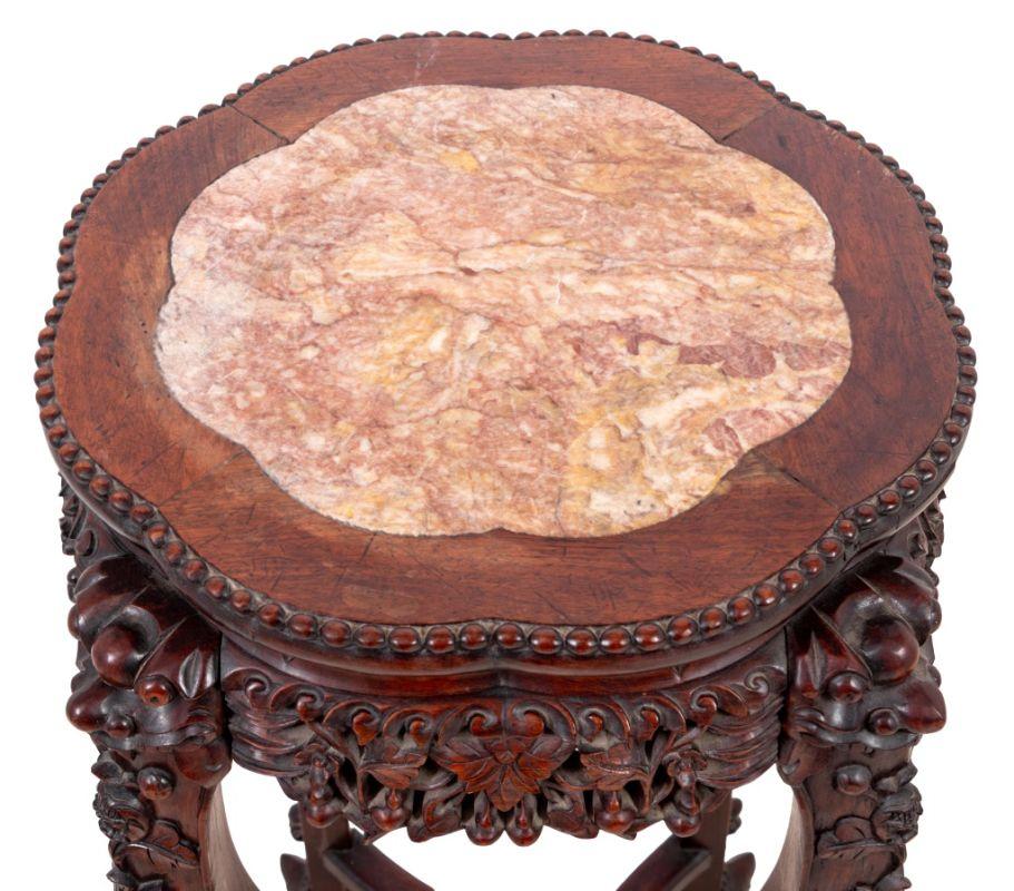 Tavolo cinese con piedistallo in legno duro intagliato e marmo, fine del XIX secolo. Il piano con inserti lobati è sovrastato da un fregio intagliato e le gambe poggiano su piedi a artiglio e a sfera, uniti da una barella a X. H. 32