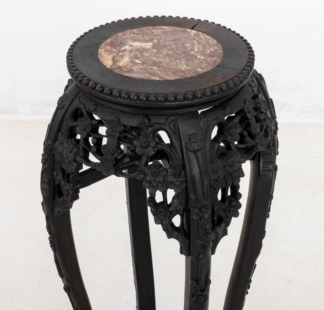 Mesa china de madera noble tallada y pedestal de mármol, finales del siglo XIX, con tablero circular sobre un friso de prunos tallados y perforados, sobre altas patas cabriolé unidas por travesaños en forma de 