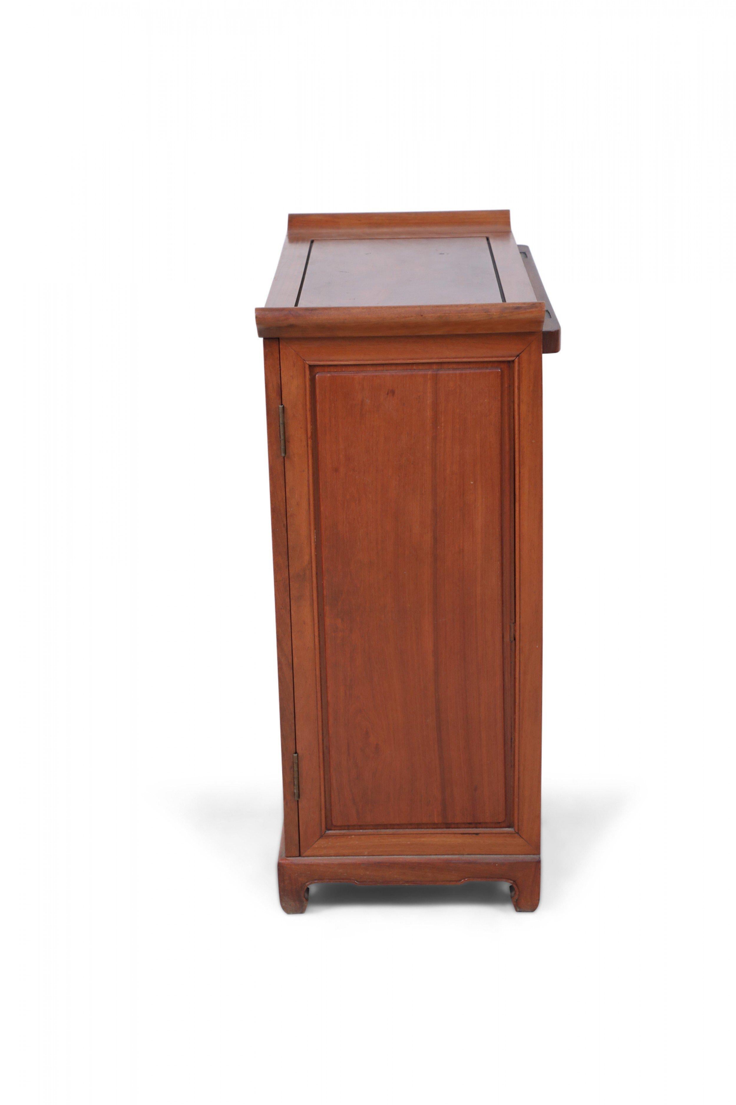 Antique Chinese hardwood bar cabinet with a paneled exterior and brass-hinged top and doors that open to reveal ample storage for glassware, slide-out bottle trays, two drawers and Shou character carvings that symbolize longevity.