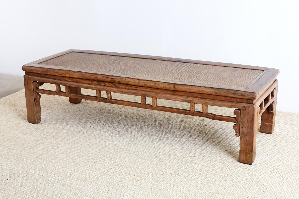 Impressive and large Chinese hand-carved bench with a woven raffia seat. Could also be used as a coffee table or low table. Features a thick carved frame with a floating top panel and humpback stretchers on all sides. The raffia top is flexible and