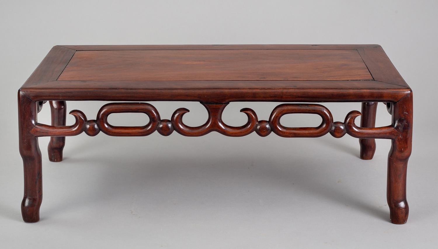 Chinese hardwood low table with a paneled top within a mitered frame, an openwork apron of linked C-scroll and oval 0 carvings joined by small spheres, raised on four shaped rounded legs.